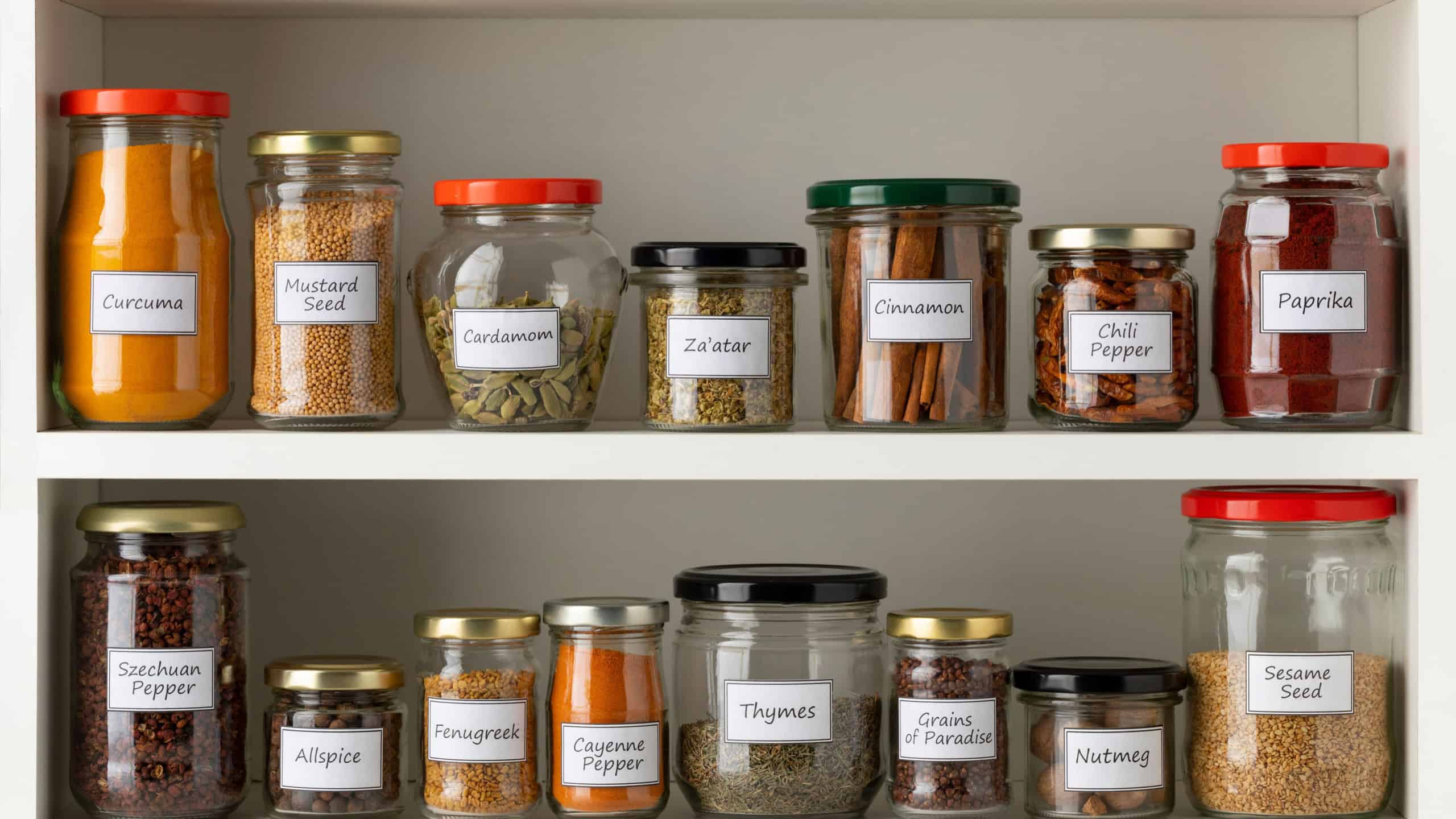 Recycled glass jars with a variety of dried herbs in a row on the kitchen shelf