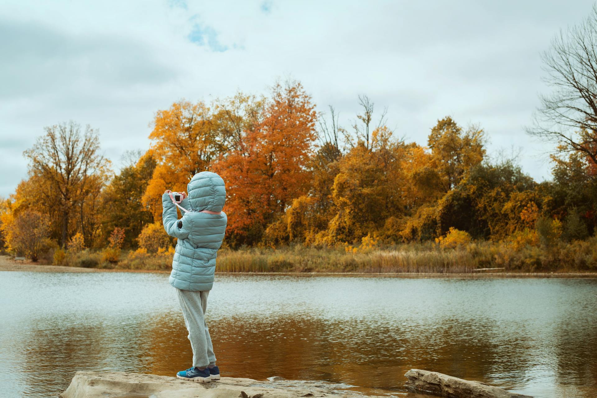 Person in Gray Jacket Standing on Brown Rock Taking A Photo