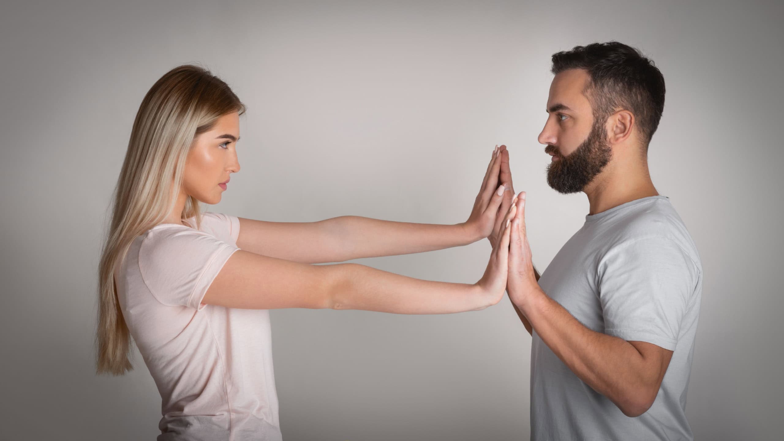 Resistance to tyranny. Girl repels with hands man claiming to her personal space on gray background, studio shot