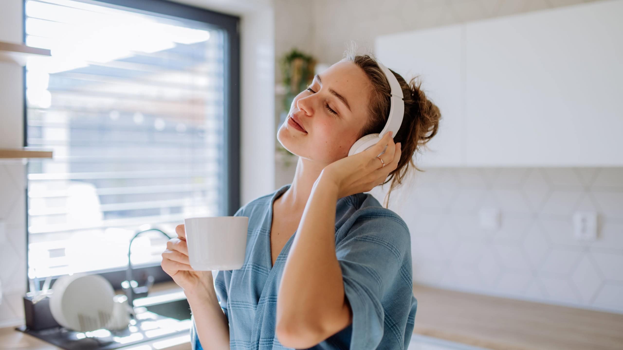 Young woman listening music and enjoying cup of coffee at morning, in her kitchen.