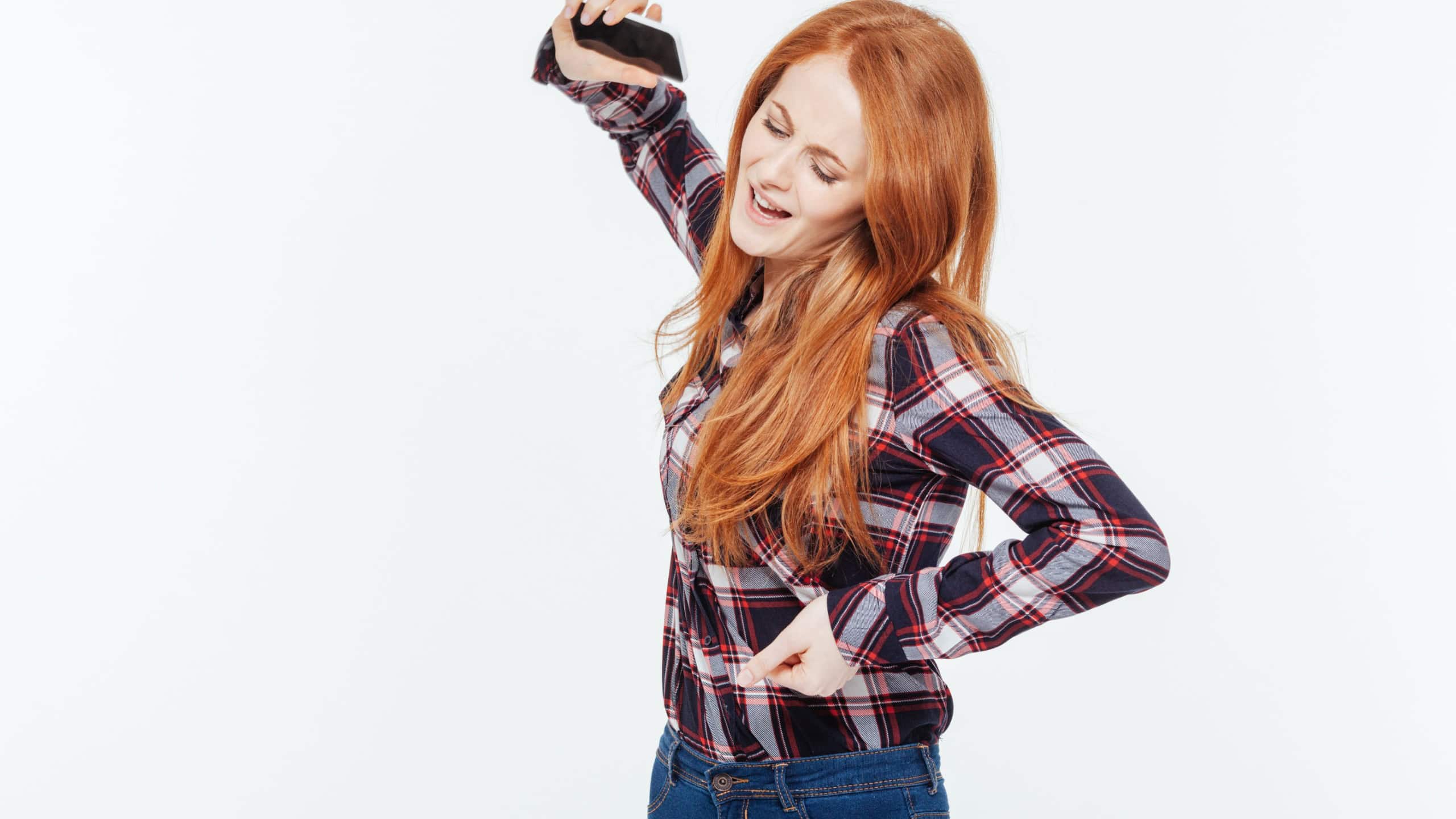 Angry redhead woman throwing mobile phone isolated on a white background