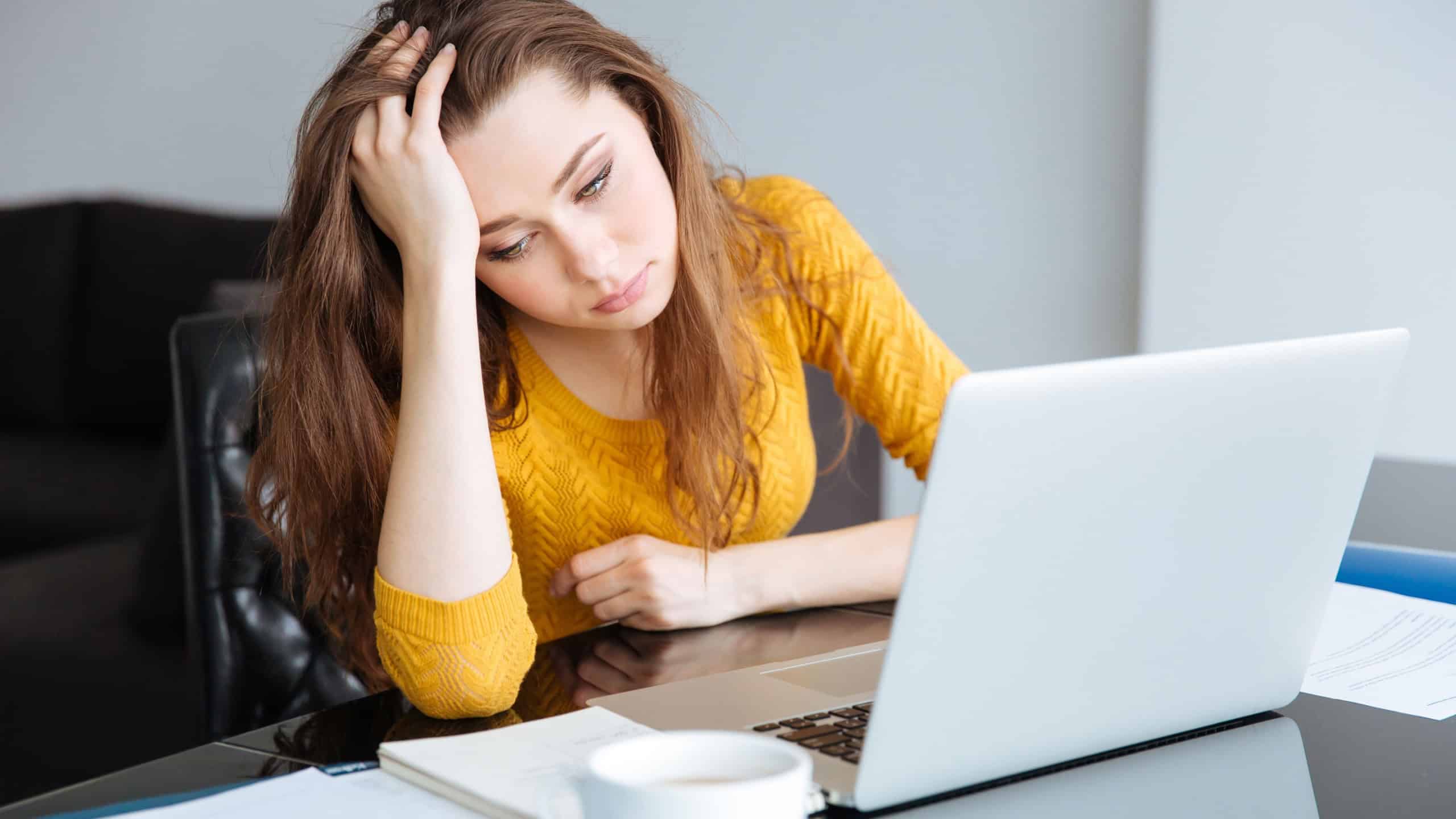 Sad woman sitting at the table with bills and laptop computer at home