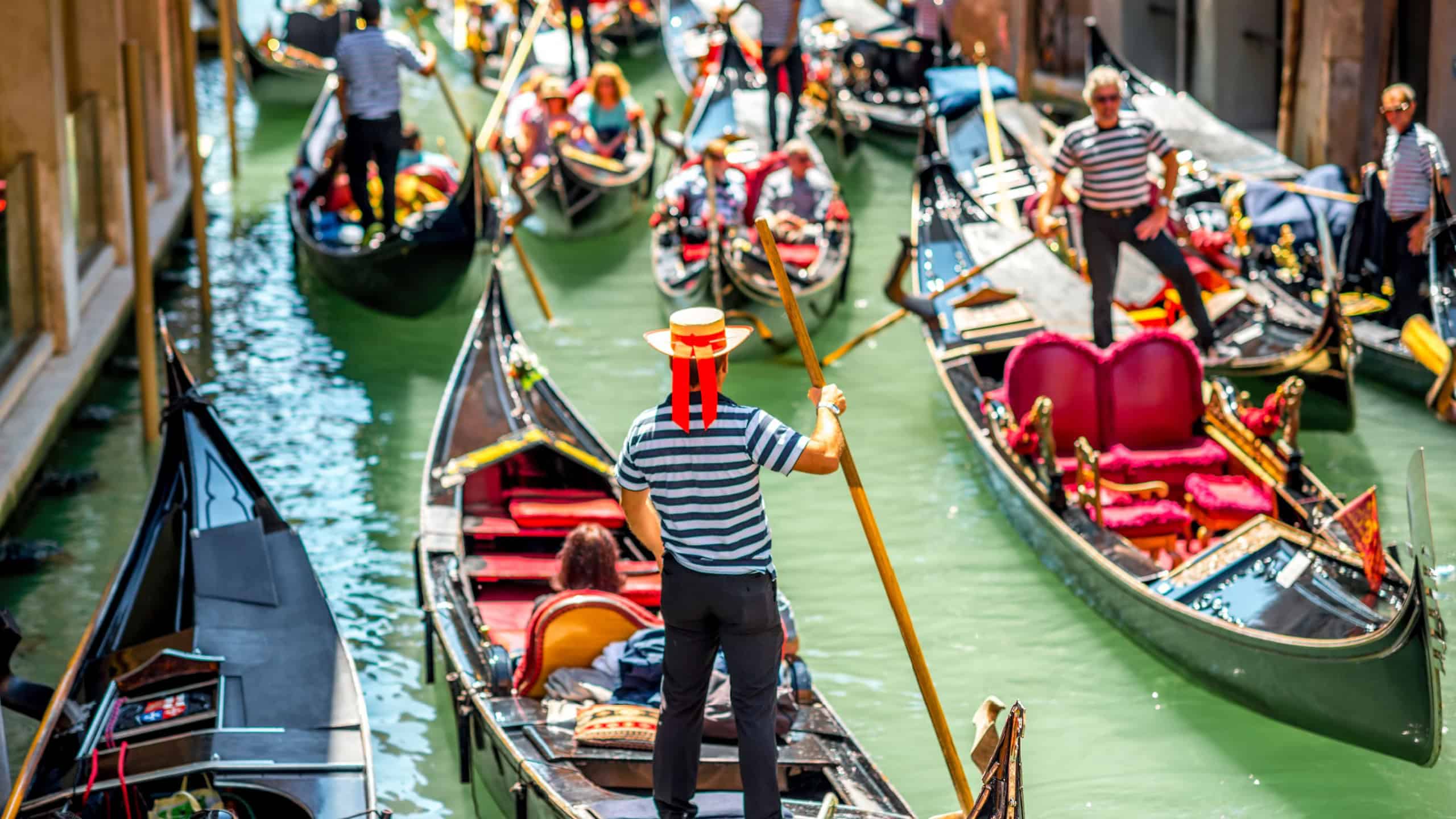 Venice, Italy - May 18, 2016: Gondoliers sail on gondolas full of tourists in the narrow water canal in Venice. Gondola is a traditional venetian boat and famous tourist attraction.