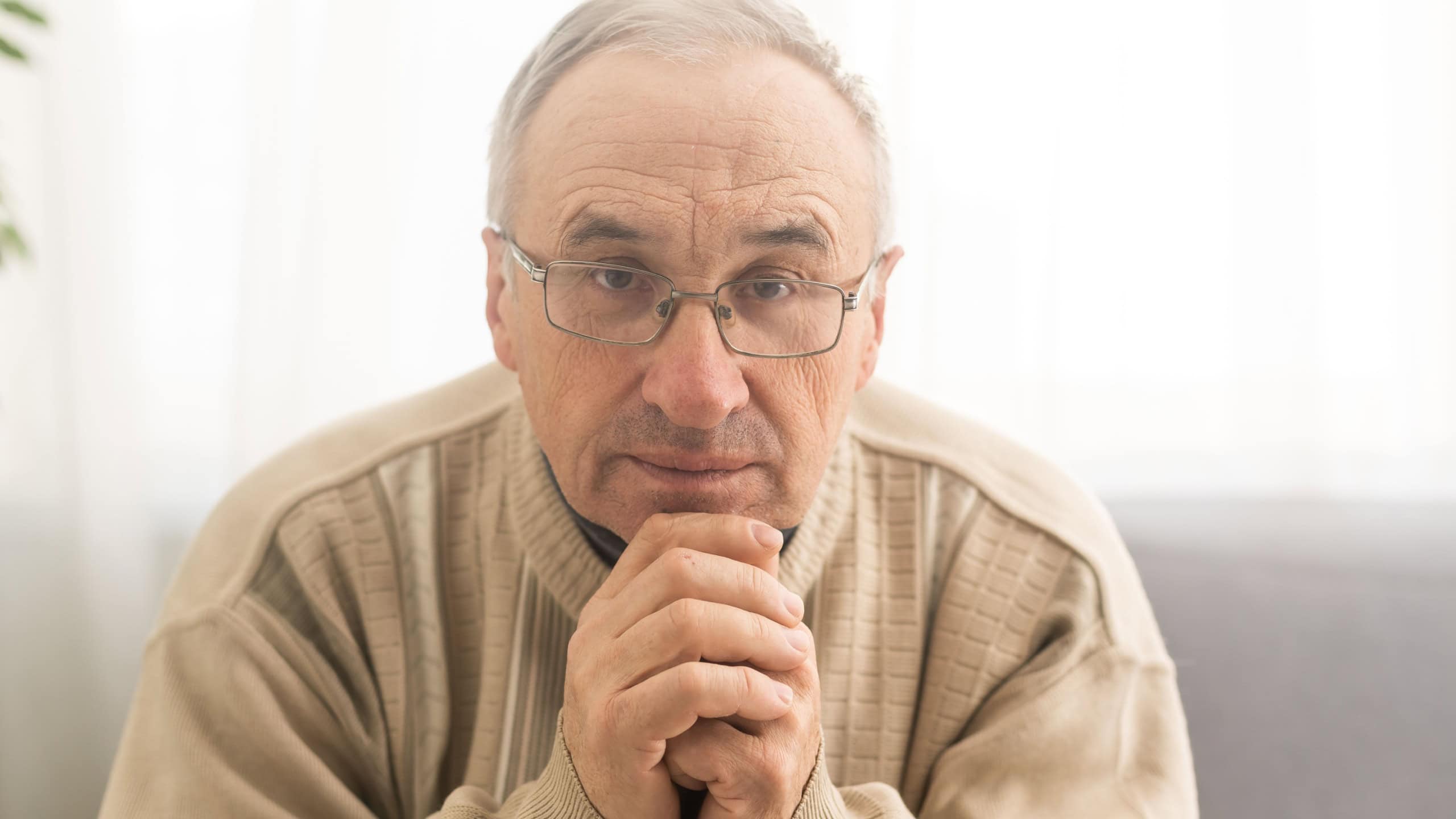 Please, Lord. Nervous worried aged Caucasian man praying on couch at home. Stressed white European senior citizen sitting on sofa, begging for forgiveness or asking God for help in difficult situation