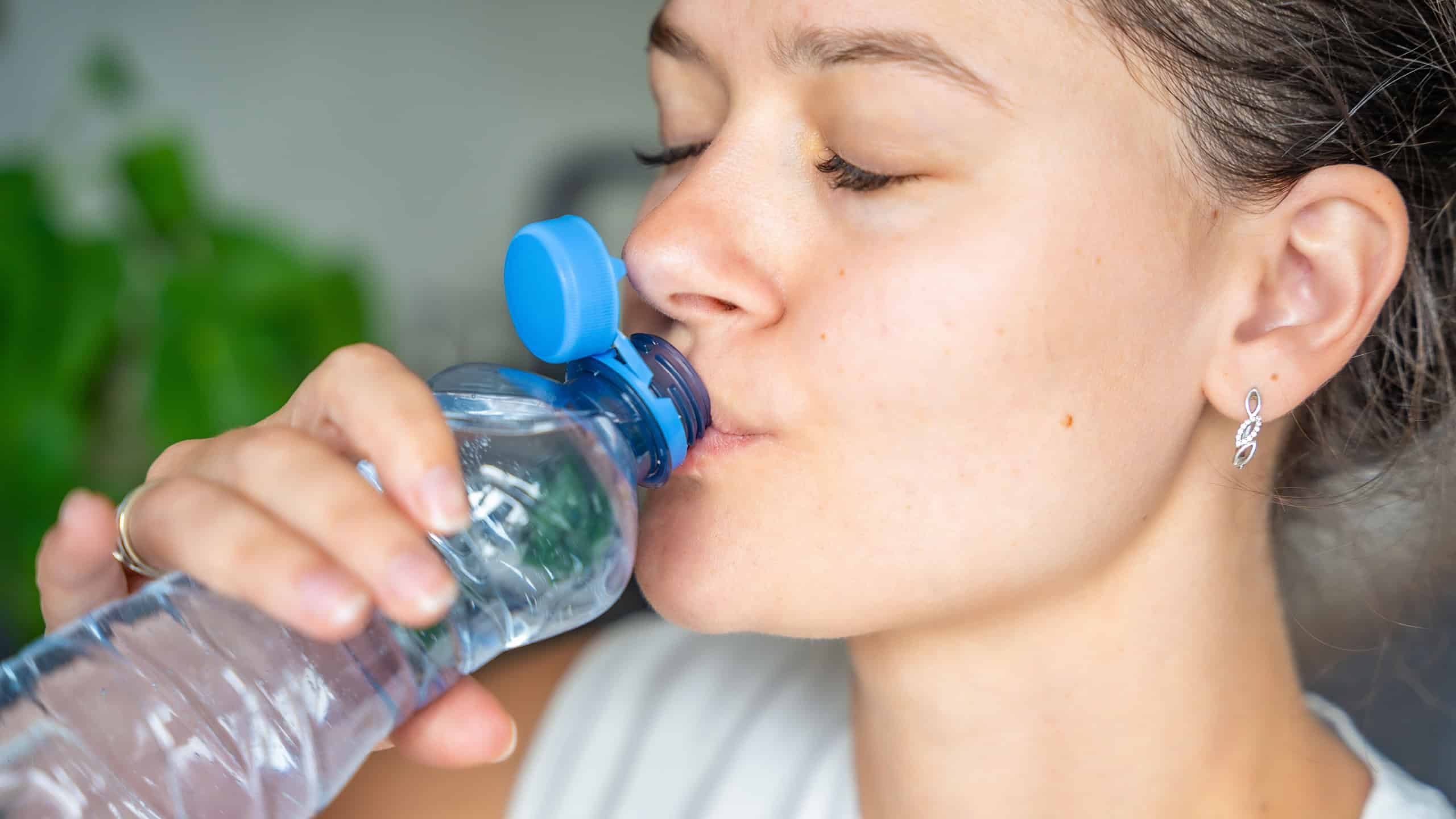 Young woman drinking from a bottle with stationary plastic cap. The new design means the cap remains attached to the bottle after opening, making the entire package easier to collect and recycle.