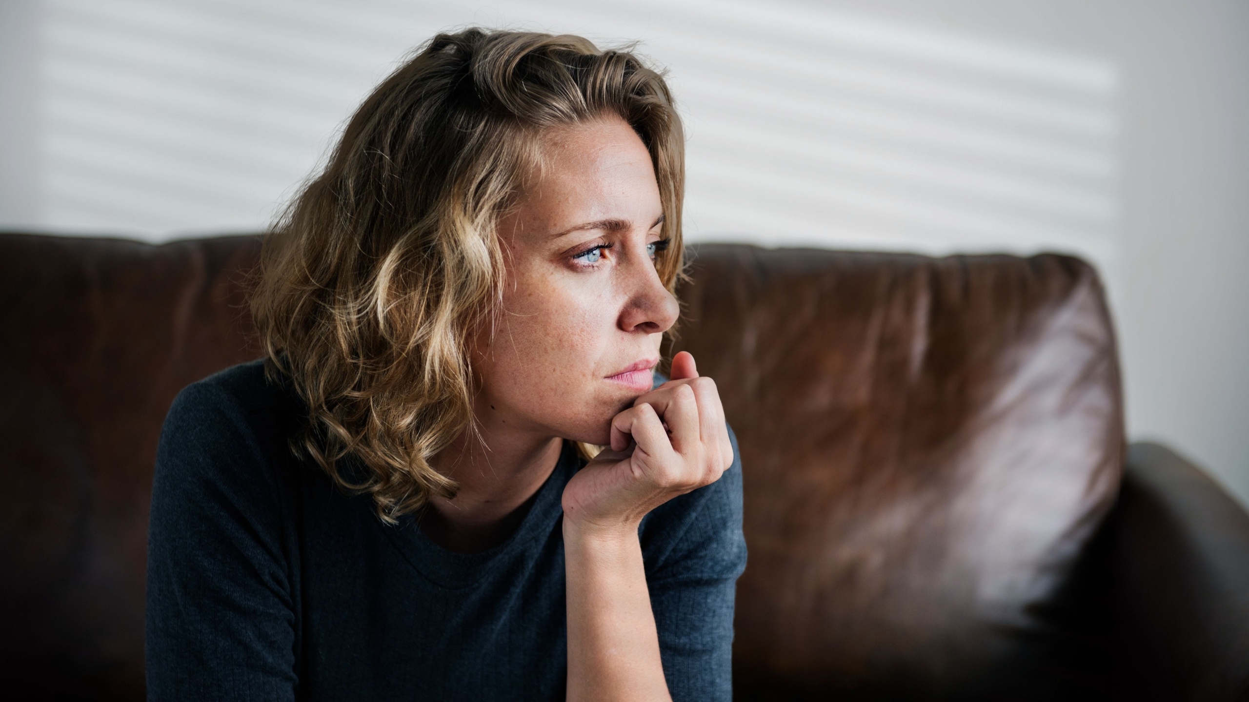 Stress woman sitting thoughtfully alone. Stress woman sitting alone on a couch. Portrait of stress woman. Stress woman in contemplative mood.