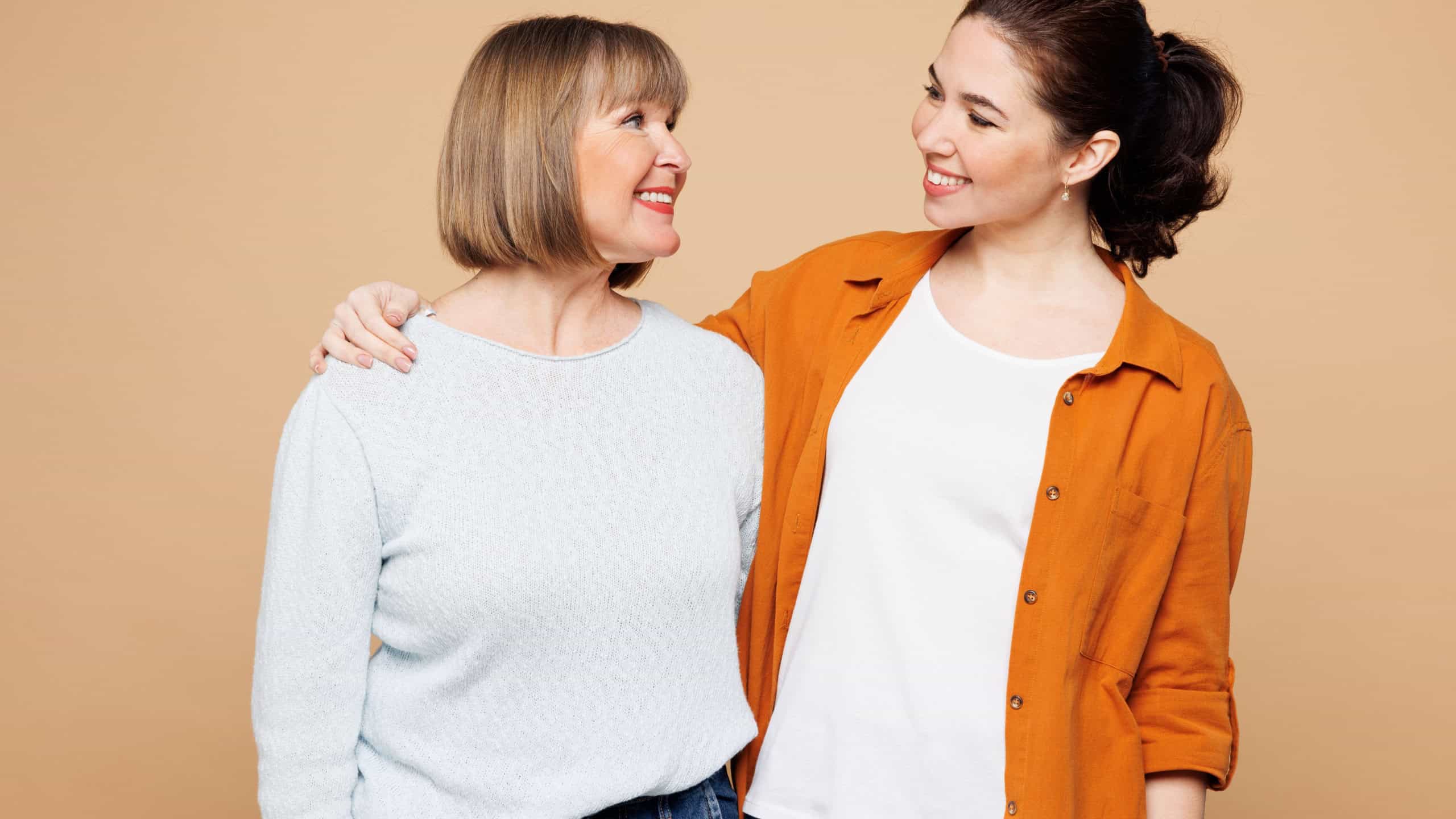 Elder smiling happy fun parent mom 50s year old with young adult daughter two women together wear casual clothes look camera hug embrace isolated on plain pastel beige background. Family day concept