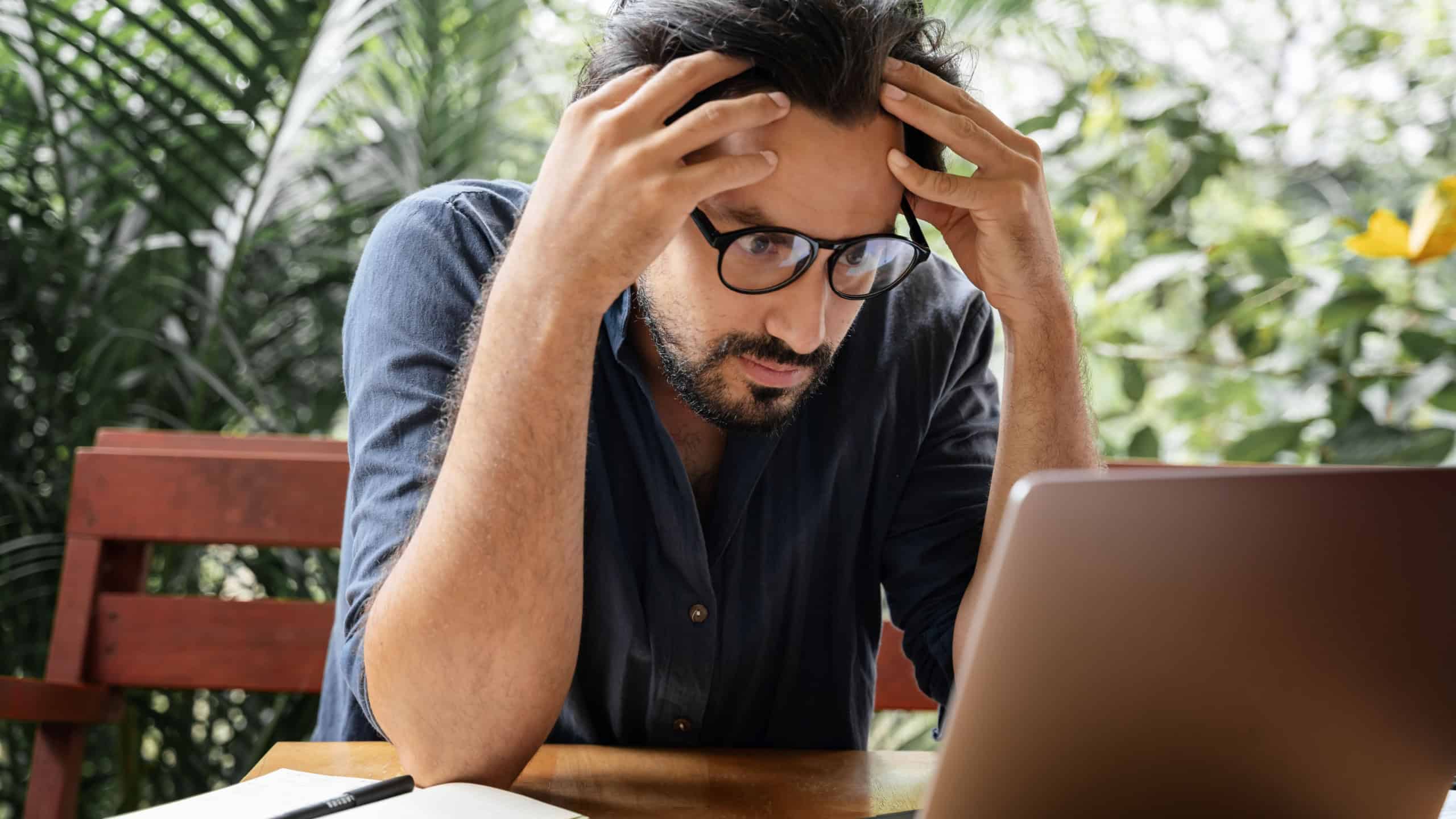 Handsome tired young curly latin man looks seriously intently at the laptop screen. Serious work, digital nomad, hard crisis, workaholism concept