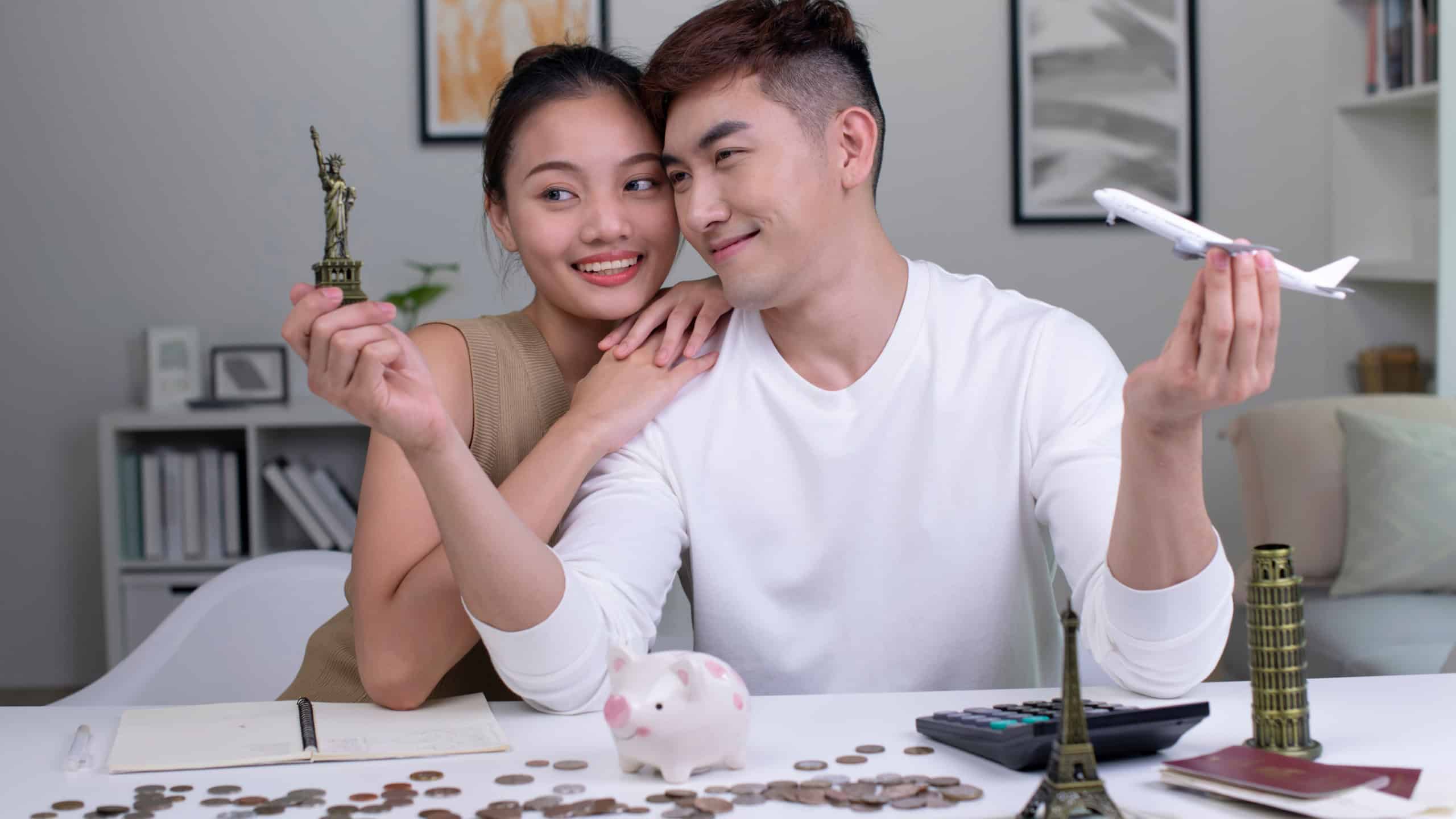 Young Asian couple plans to save money for a trip around the world. Travel budget concept. passport, monument model and aircraft toy in the picture.