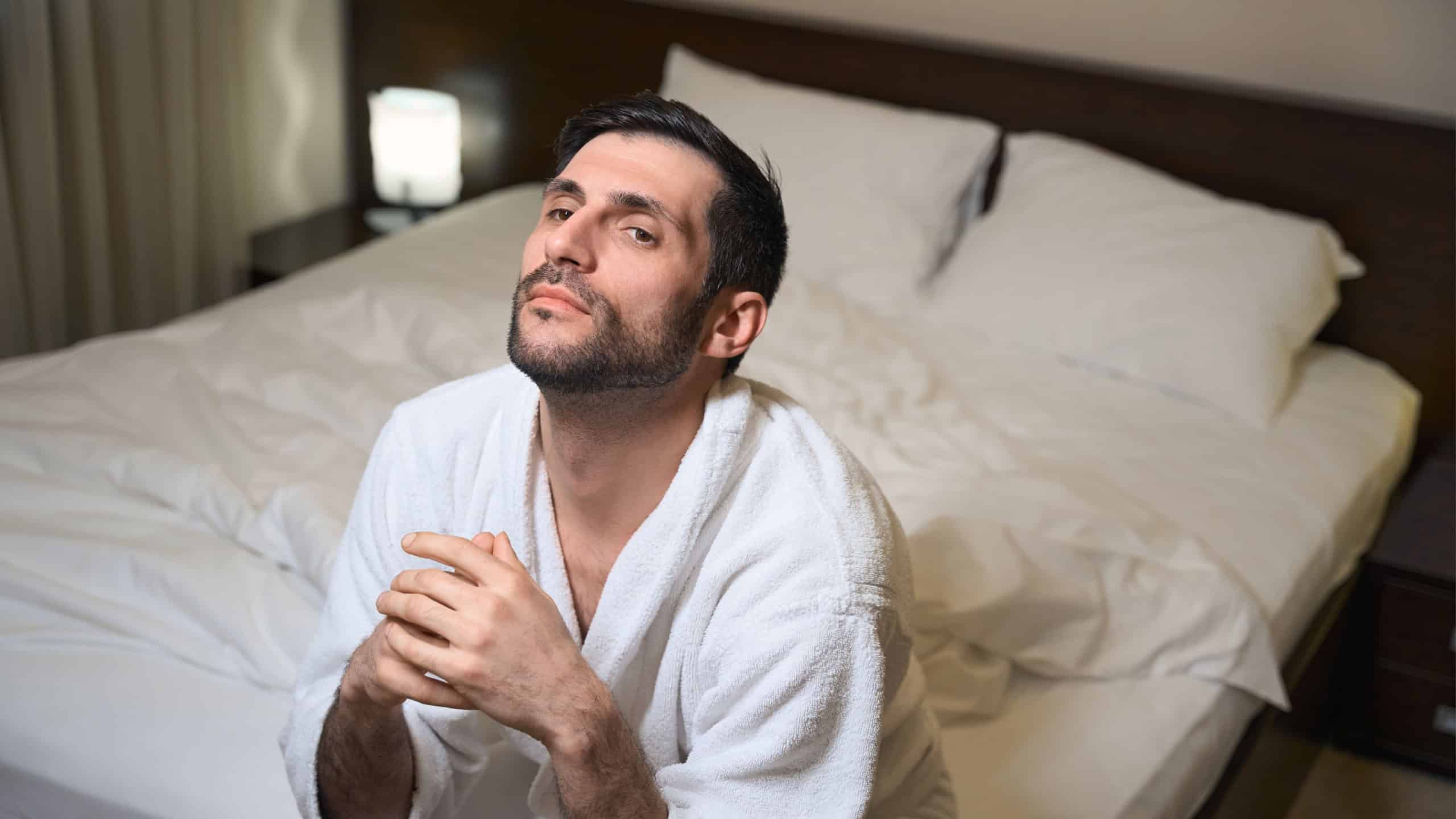 Sad man is sitting on a bed in hotel room