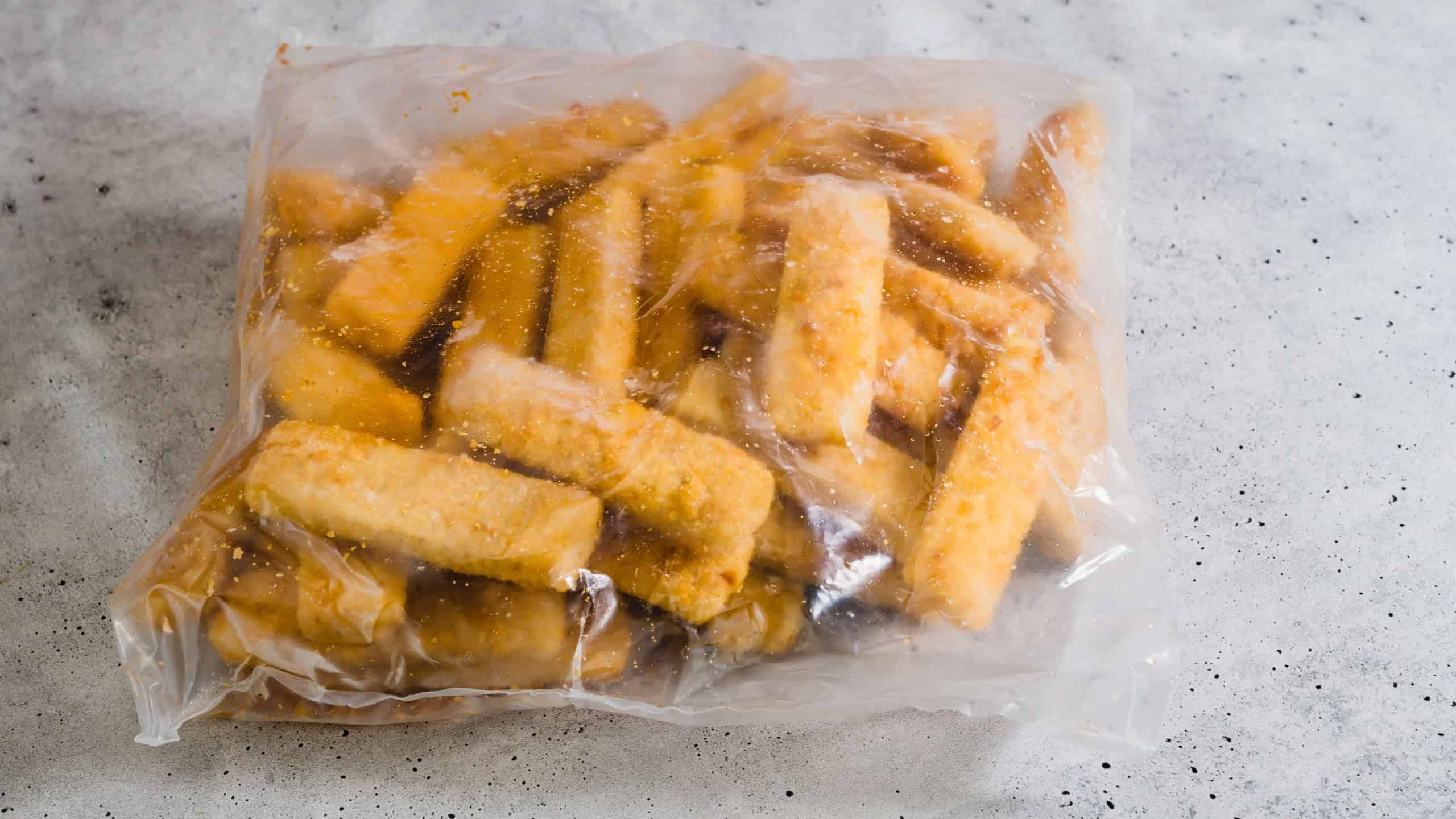 Bag of frozen breaded fish sticks close-up on grey stone background