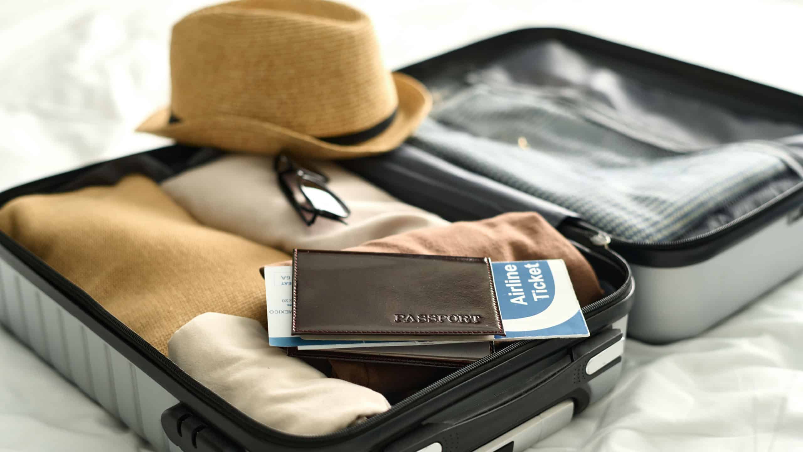 Background image of open suitcase with passport and airplane ticket on bed in hotel room travel concept