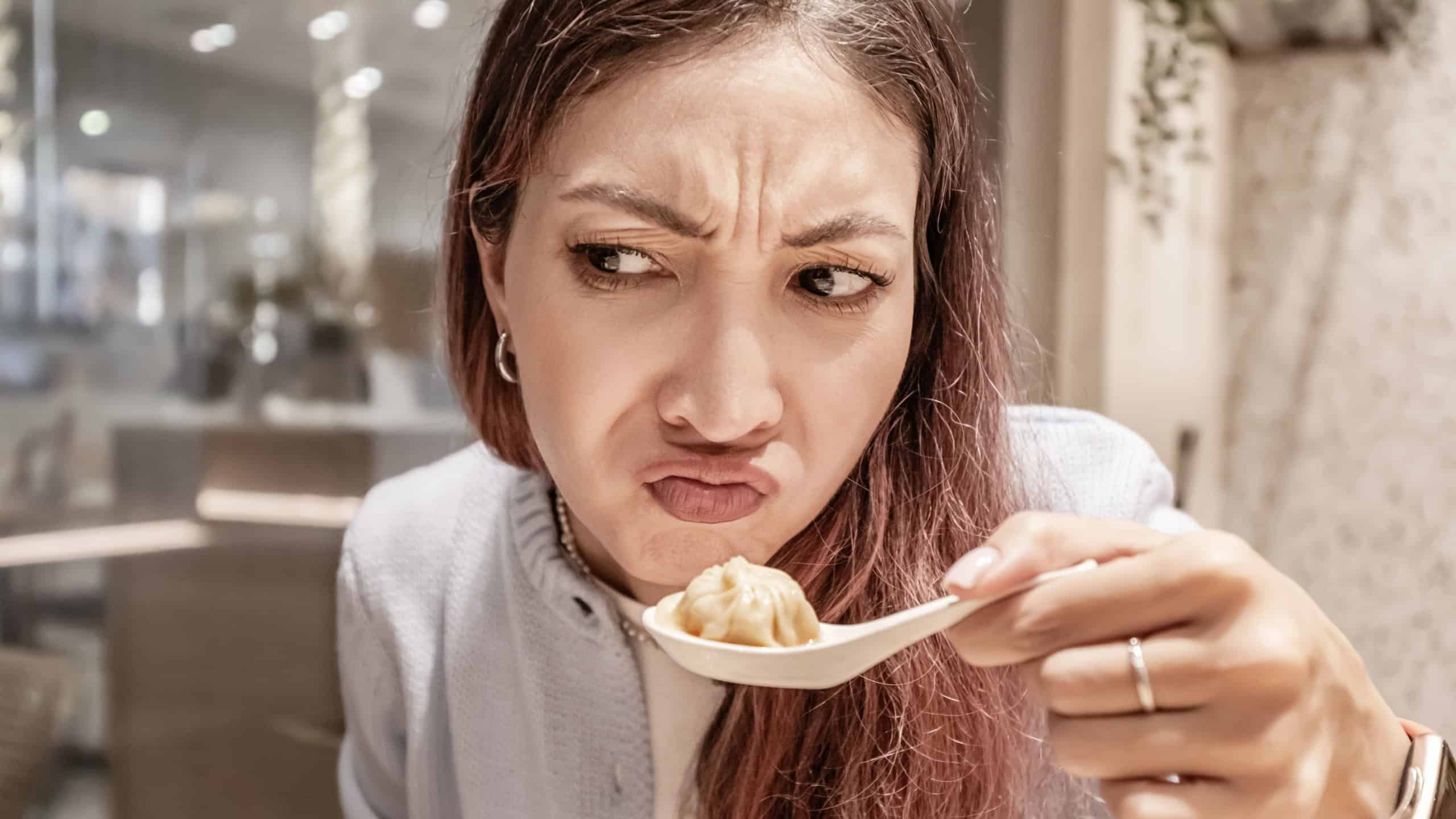 Young woman making a disgusted face while holding a spoon with a dumpling in a chinese restaurant