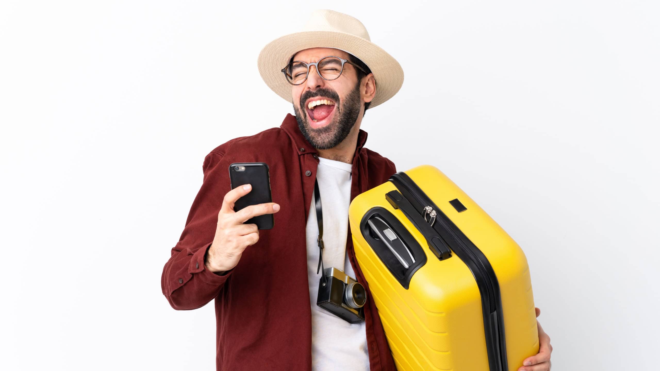 Traveler man man with beard holding a suitcase over isolated white background with phone in victory position