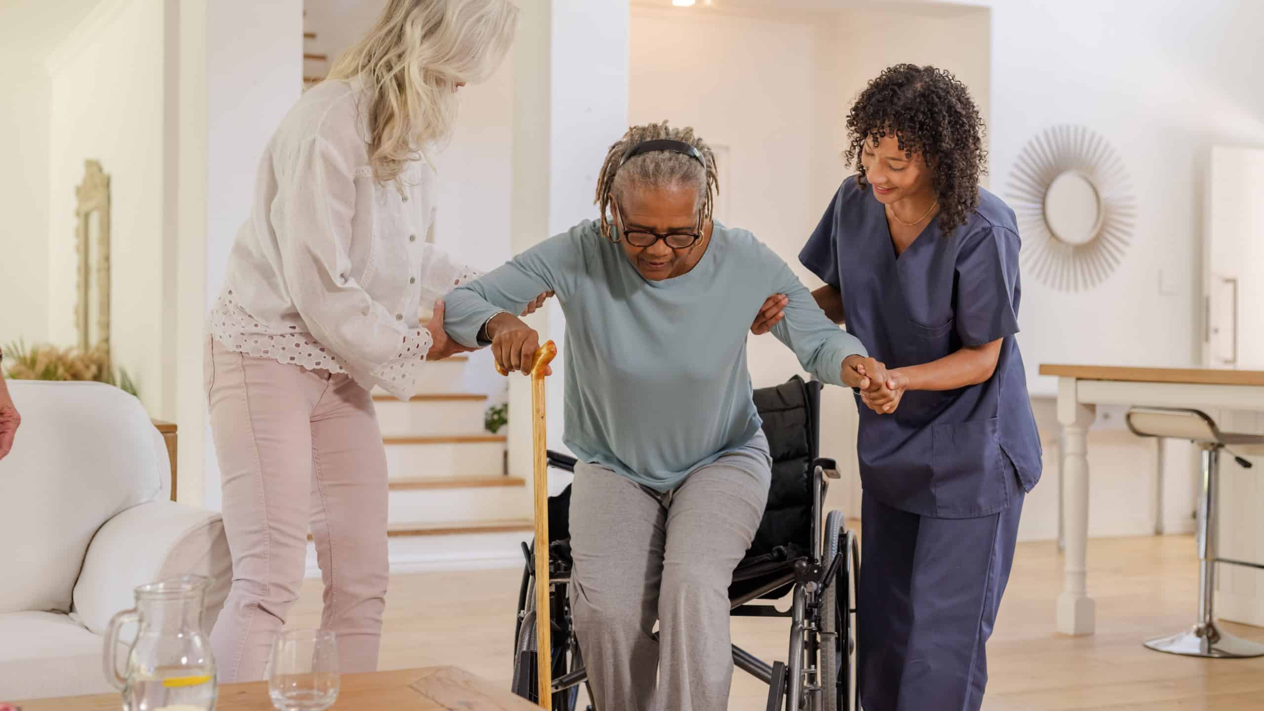 Assisting African American senior woman, caregivers helping transition from wheelchair at home. Caregiving, elderly, support, assistance, healthcare, mobility