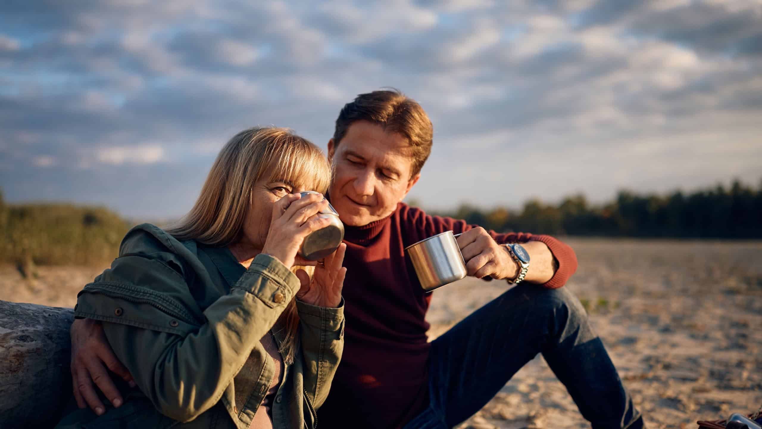 Happy mature couple enjoying while drinking tea in nature in autumn. 