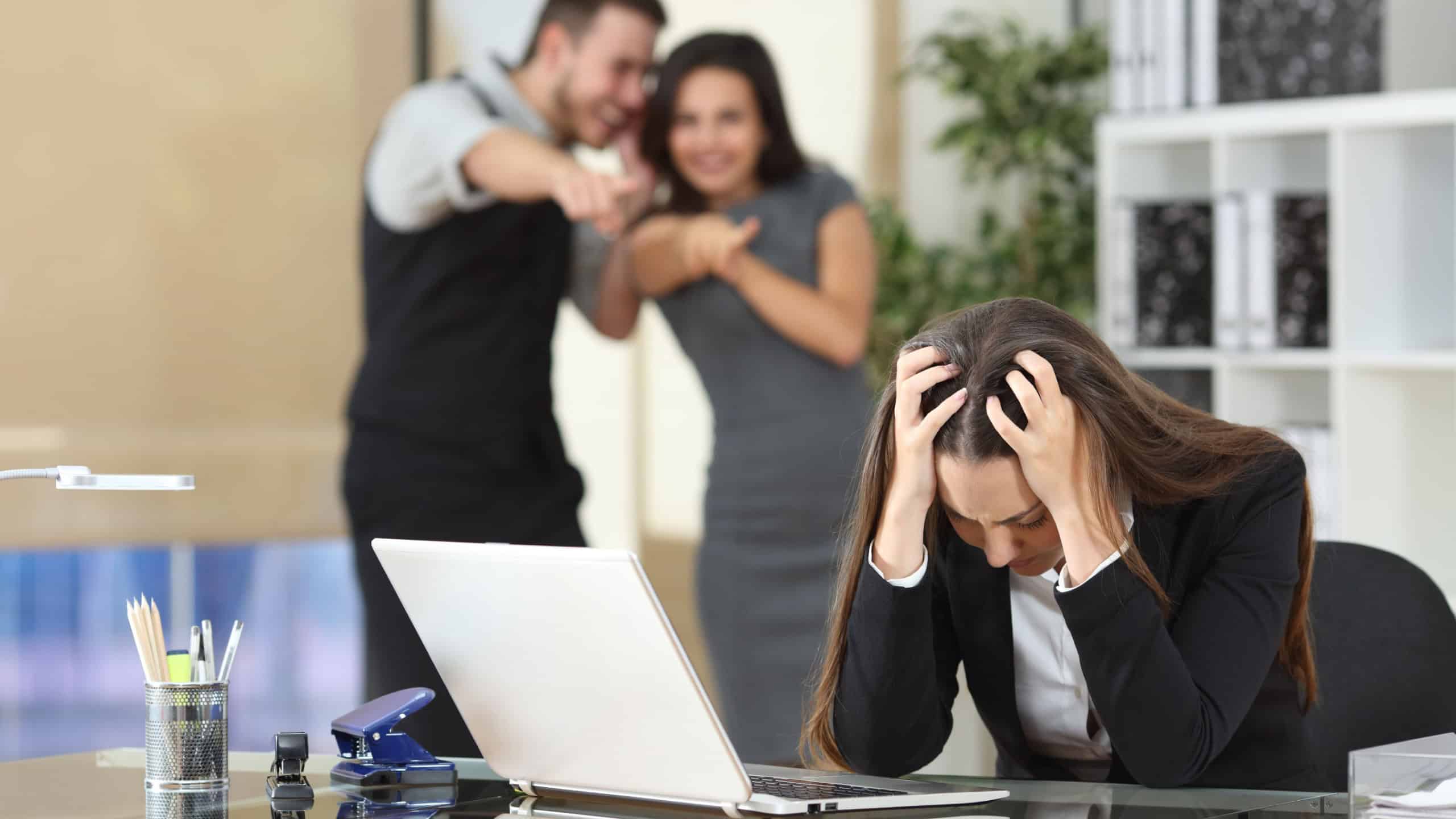 Two businesspeople bullying a sad colleague that is sitting in her workplace at office