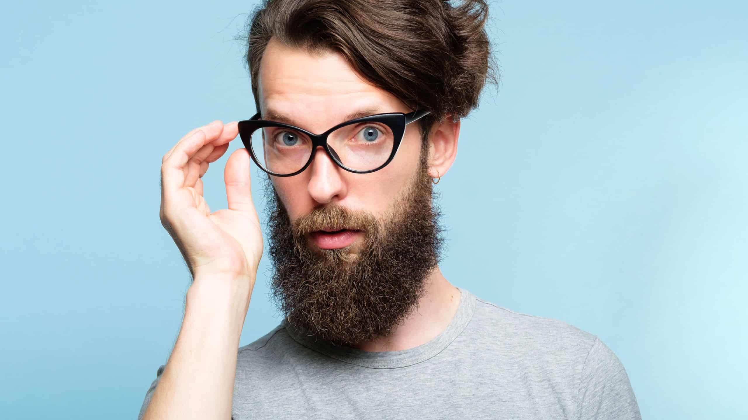 eccentric teacher or quirky it guy. bearded hipster dude wearing cat eye glasses. stylish modern fashionist. portrait of a geeky foppish man on blue background.