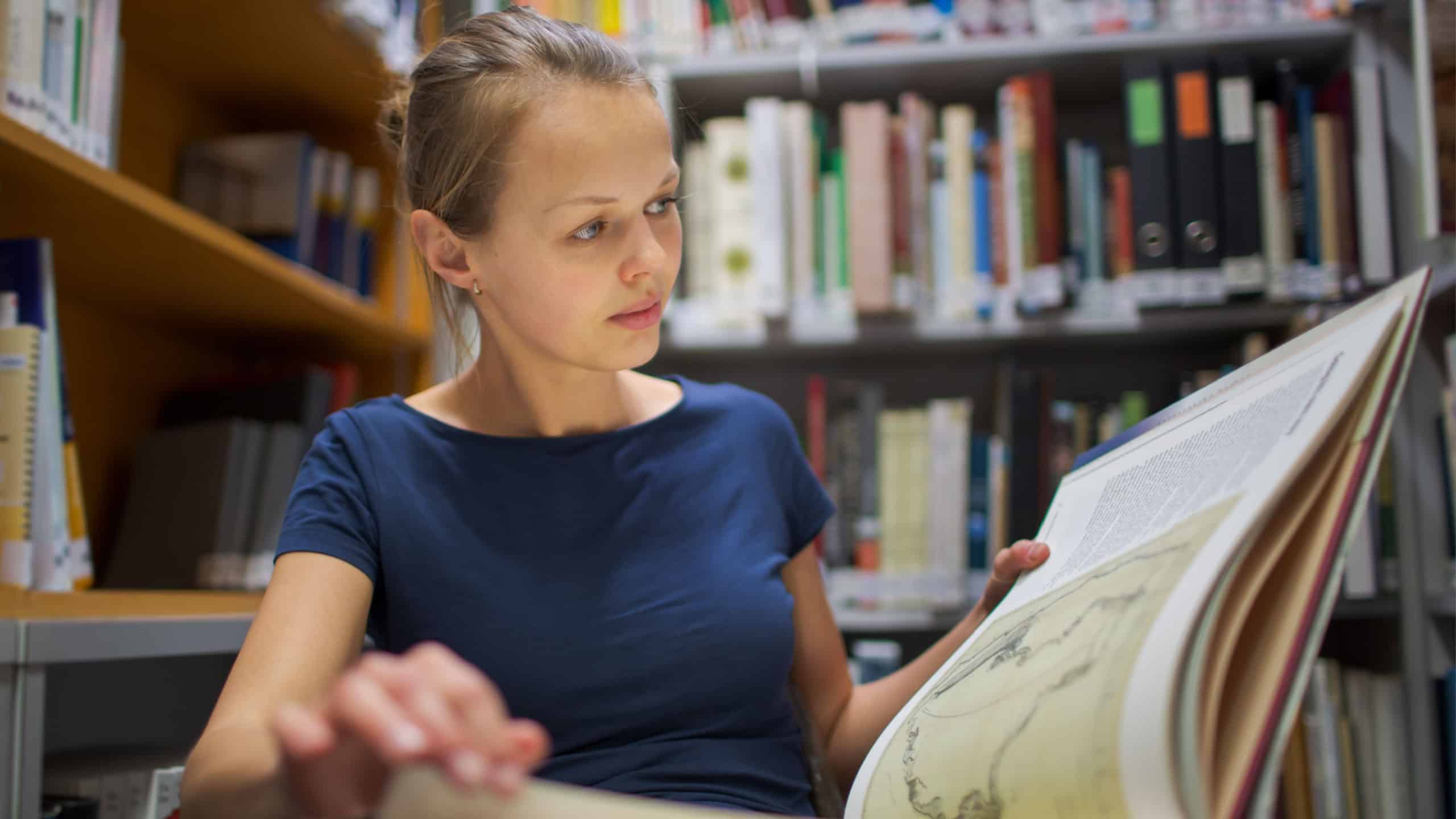 Pretty, young woman studying an old book in archives