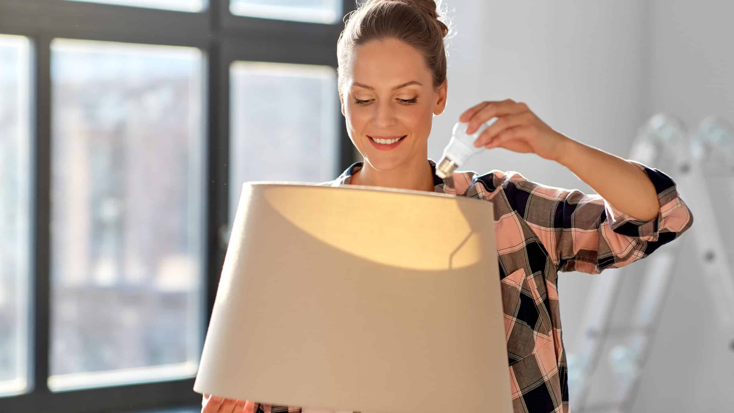 moving, electricity and repair concept - woman changing light bulb in floor lamp at new home