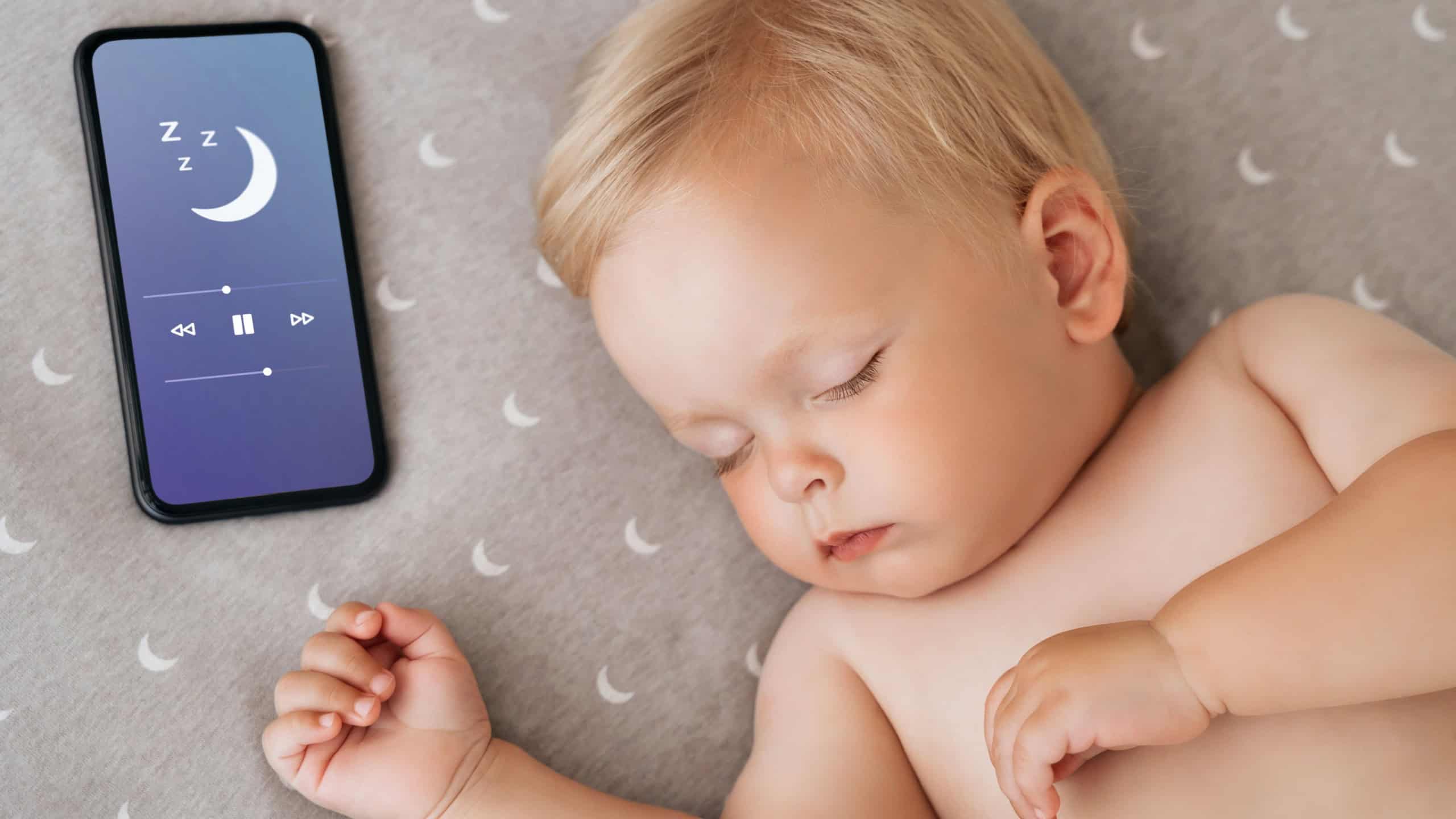 Closeup portrait of cute little boy watching sweet dreams in his bed falling asleep with music playing in app for baby sleep on phone lying next to his head. Happy maternity and technology