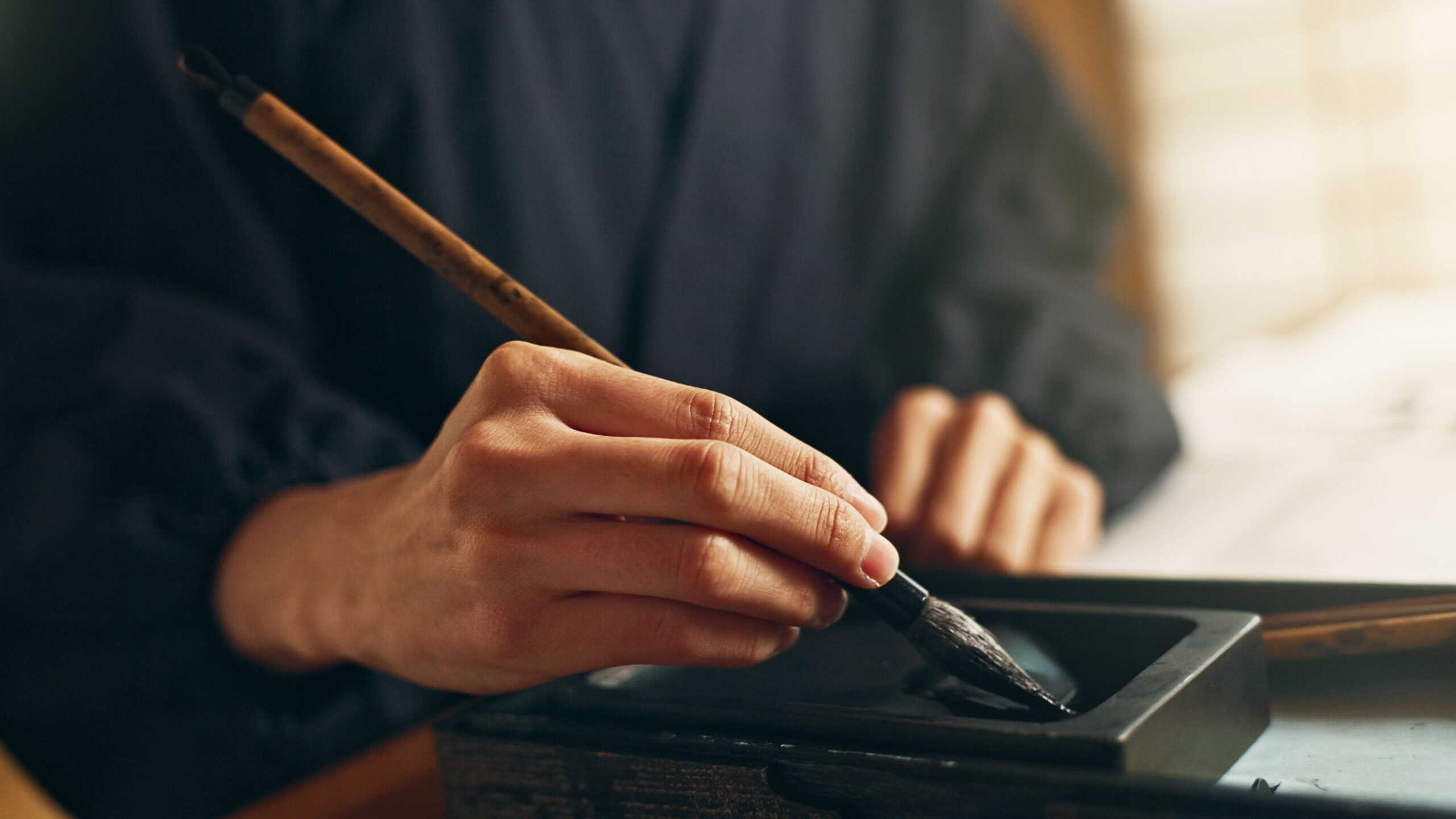 Hands, reed pen or brush in ink for writing, calligraphy or ancient script for art and inkstone. Japanese creativity, black paint and vintage tools, paintbrush and stroke, traditional and stationery