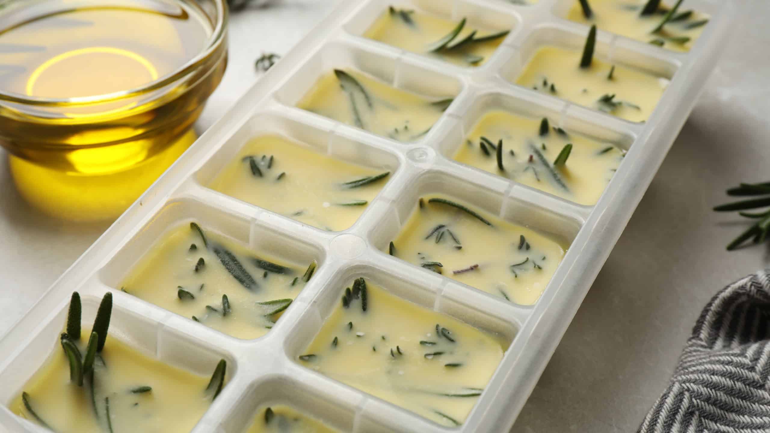 Ice cube tray with herbs frozen in oil and fresh rosemary on grey table, closeup