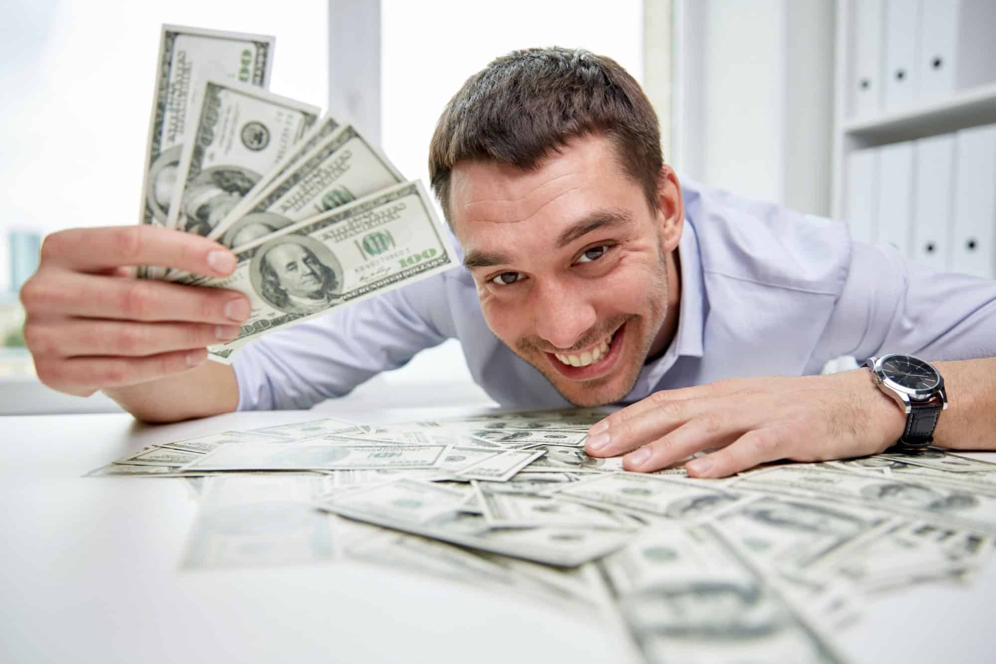business, people, success and fortune concept - happy businessman with heap of dollar money in office