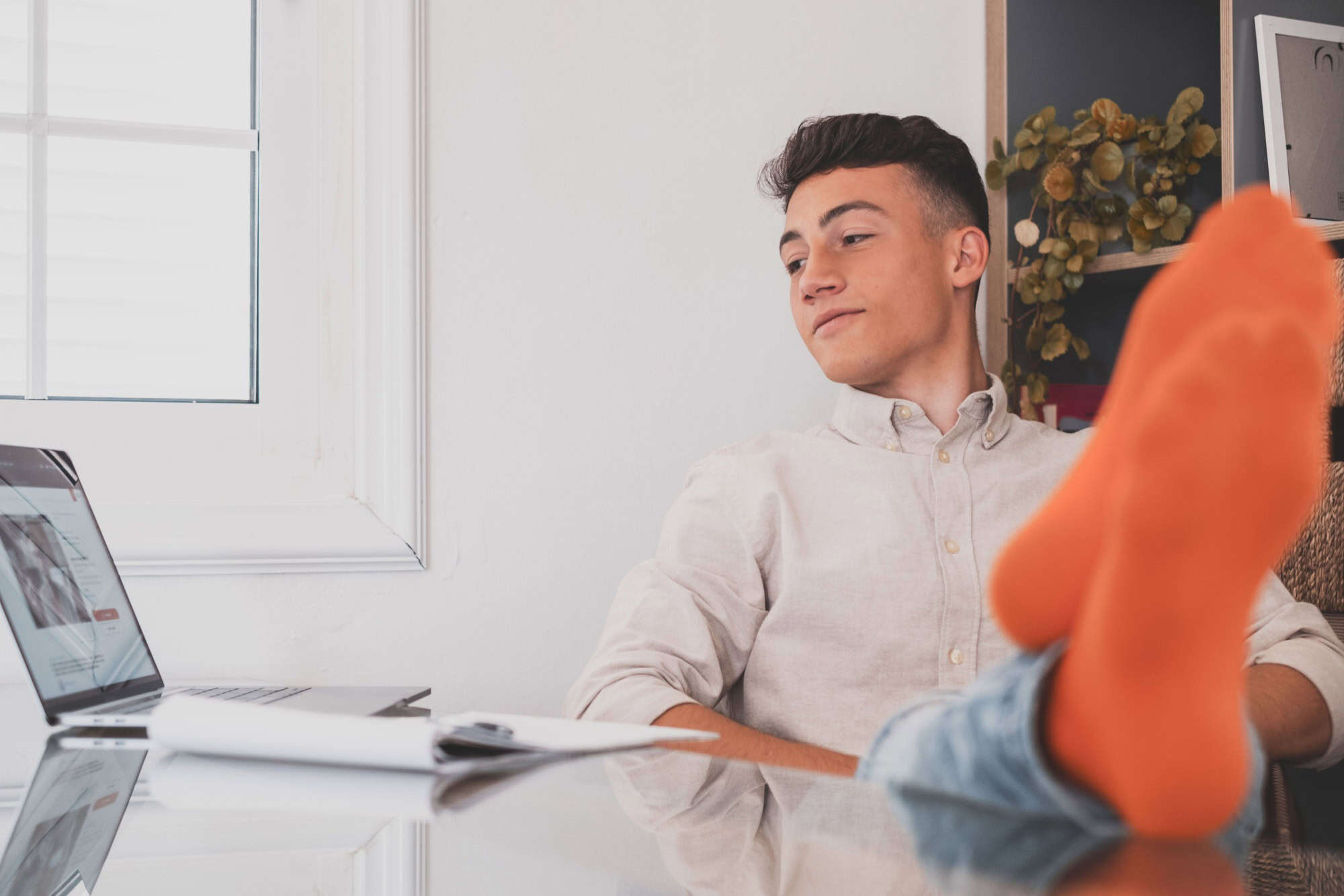 Satisfied teenager happy to finish work with laptop at home, raises hands and puts feet up on table, relaxing after hard working day in expectation of weekend leave, relaxed workday, no stress