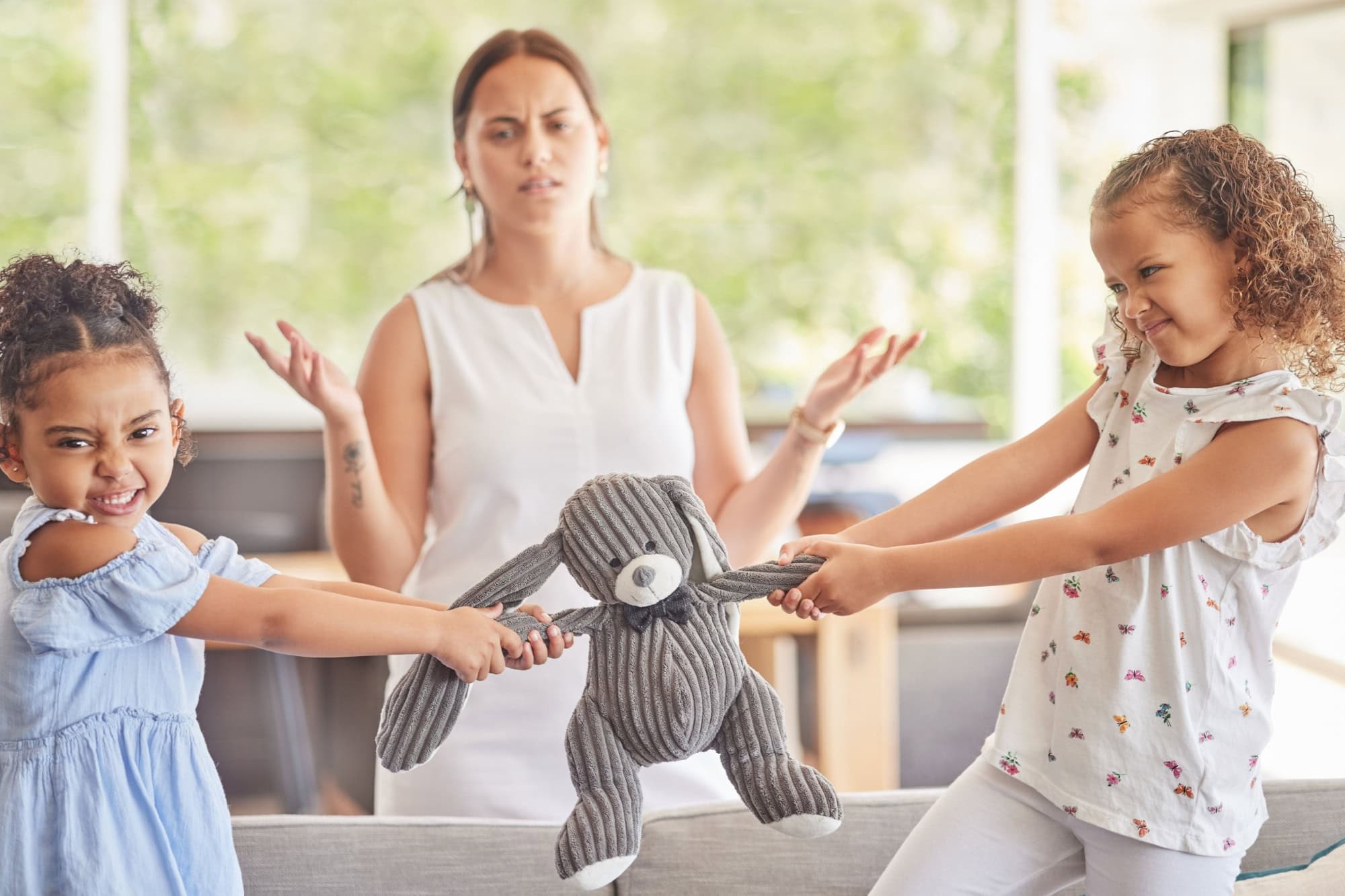 Toys, fight and kids with angry children in conflict while mother confused about family problems or communication. Girl siblings upset about teddy bear with mom trying to talk in home living room