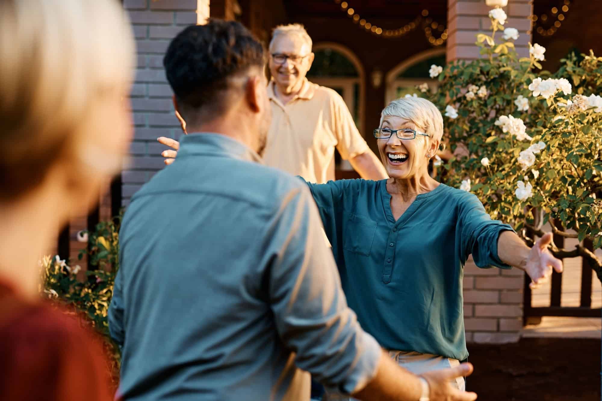 Happy senior couple welcoming their son and his wife who came to visit them. Focus is on senor woman.
