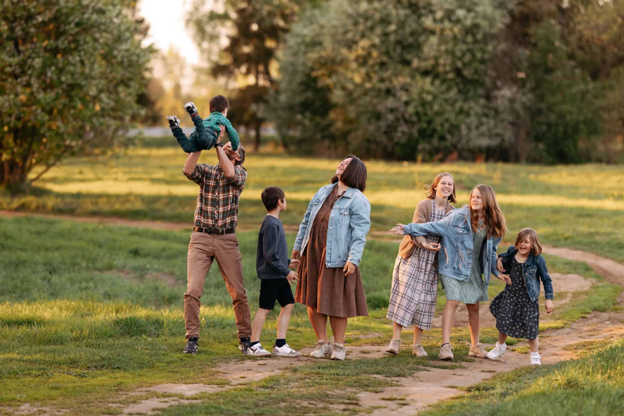 A large family consisting of a father, mother, two brothers and three sisters are happily walking in a field in the summer, full-length portrait. Children are running.