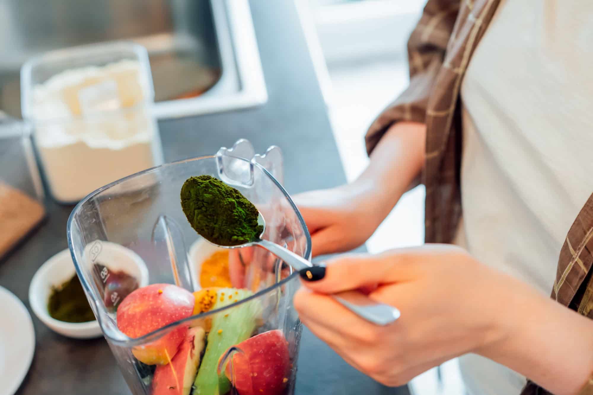 Close up woman adding spirulina or chlorella powder during making smoothie on the kitchen. Superfood supplement. Healthy detox vegan diet. Healthy dieting eating, weight loss program. Selective focus