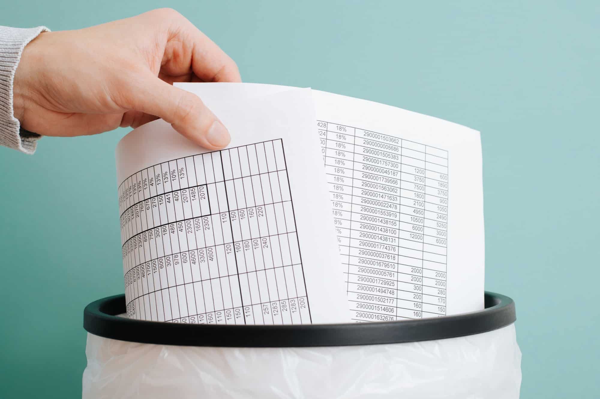 Worker throwing away documents reports bills in trash can, close-up of hand and sheets of paper.