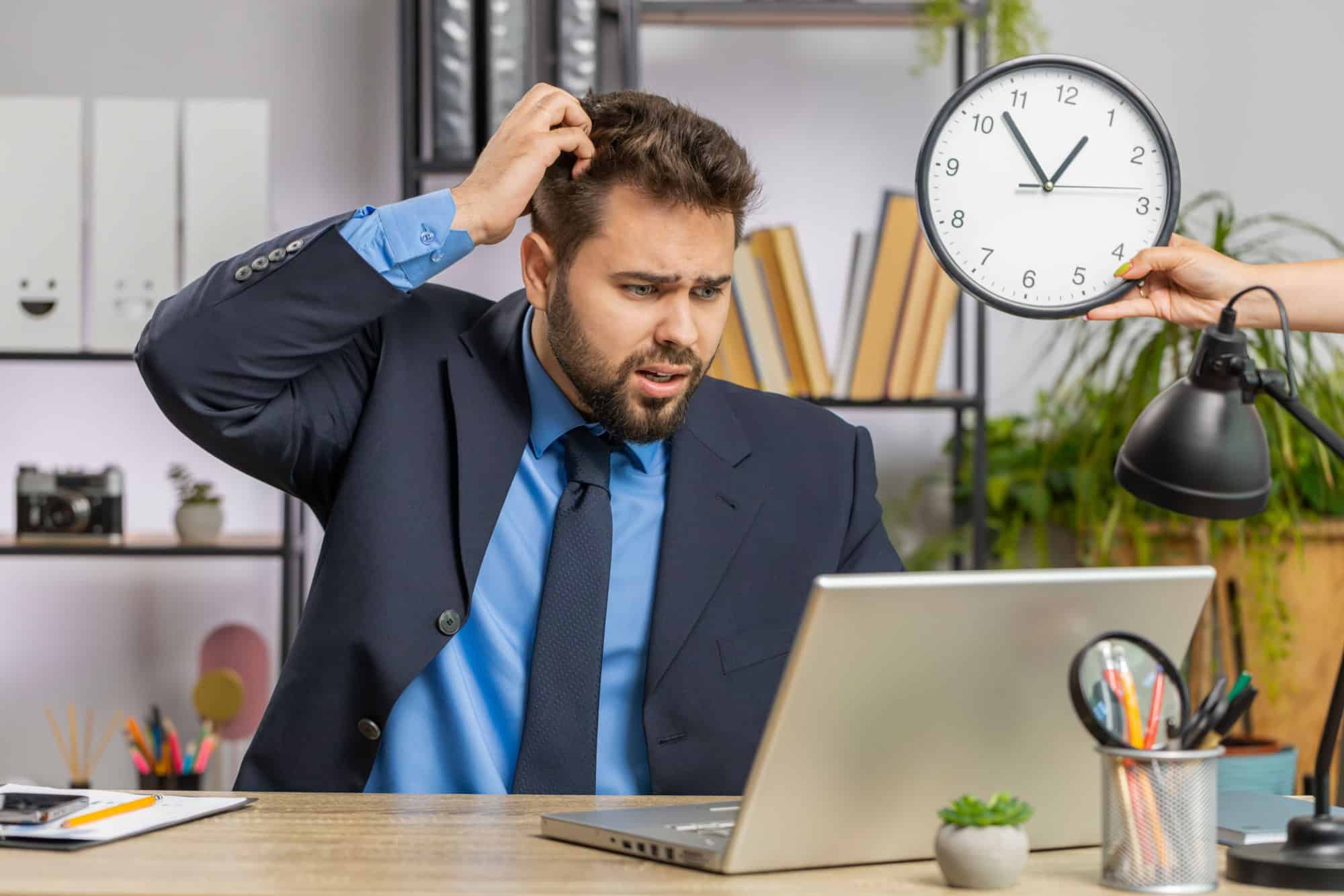 Caucasian businessman working on office laptop with anxiety checking time on clock running late to work being in delay deadline. Manager freelancer man looking at hour, minutes worrying to be punctual