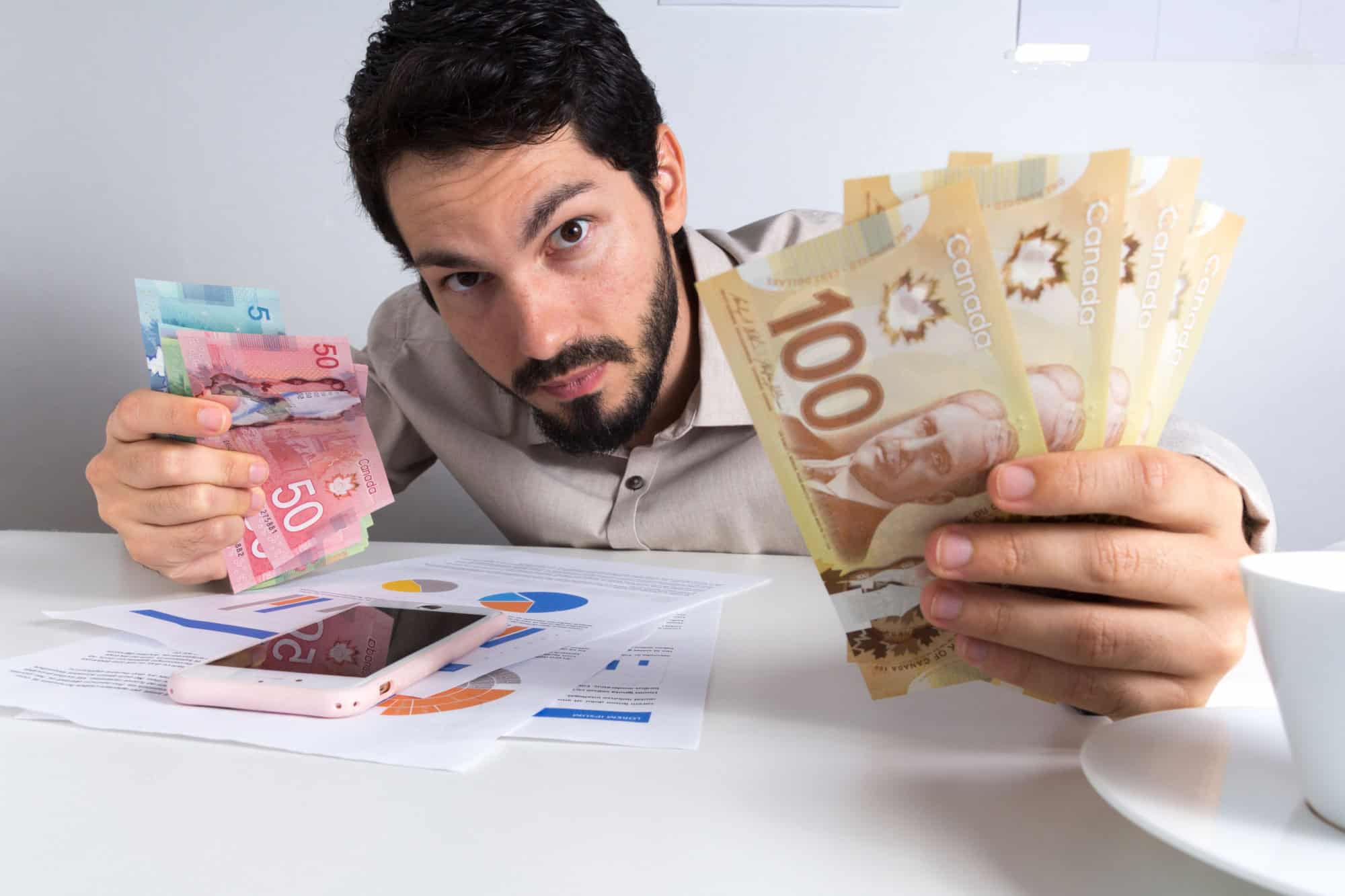 Paper notes from Canada. Dollar. Canadian cash. Young adult holding many bills on table.