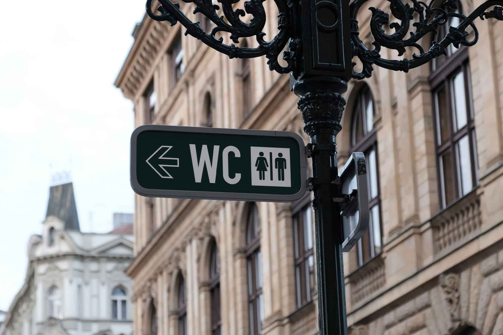 WC sign, logo of public toilets in the street against building background. For female, male. Public toilet sign on vintage street light pillar. Street lamp with wc symbols in downtown