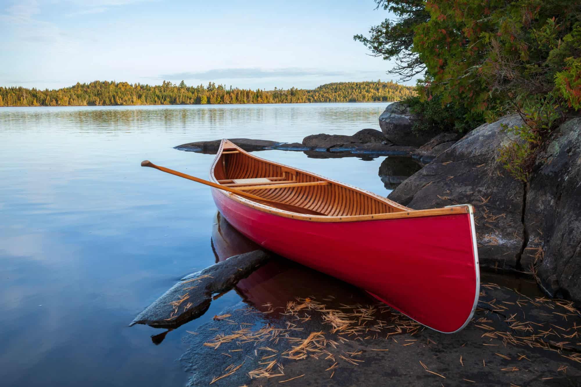 Red wood canoe on rocky shore of a Boundary Waters lake in morning light during autumn