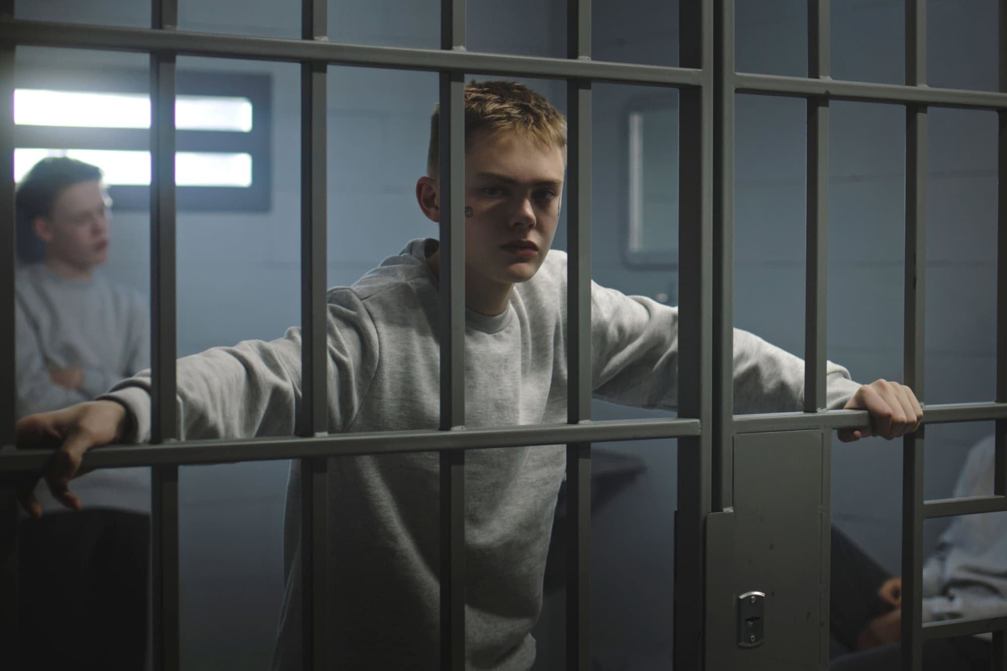 Portrait of diverse teenage prisoners behind metal bars in prison cell looking at camera. Multiethnic young inmates serve imprisonment terms in jail. Juvenile detention center or correctional facility