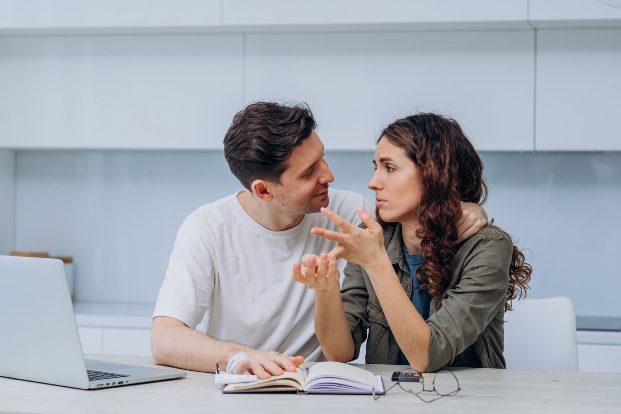 Young couple discussing finances at home with laptop and notebook. Man supports woman who is worried about the lack of money. Family care.