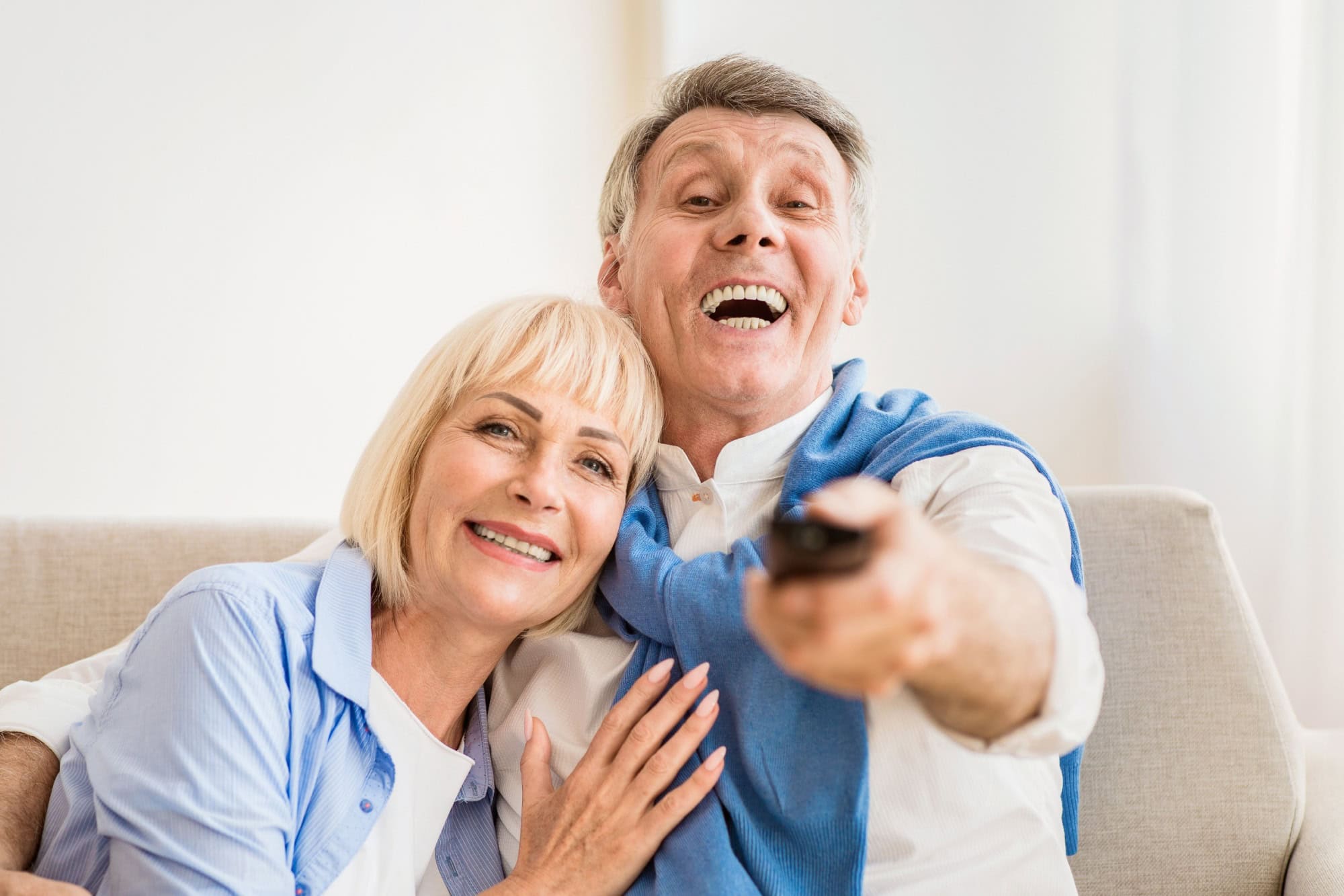 Watch tv. Excited mature couple switching channels with remote controller, resting at home