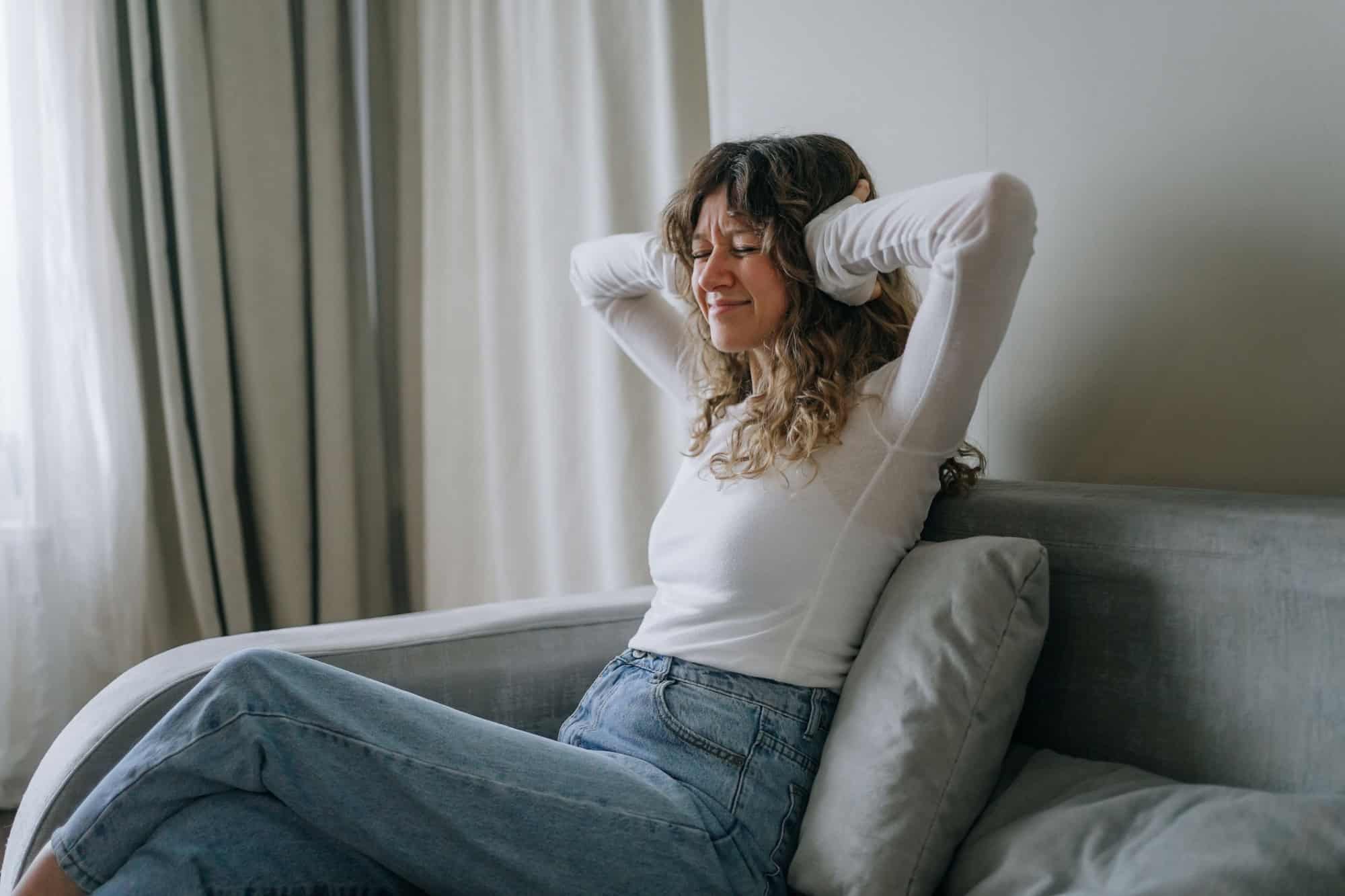Stressed woman on sofa covering ears from loud noise, feeling annoyed and frustrated in living room