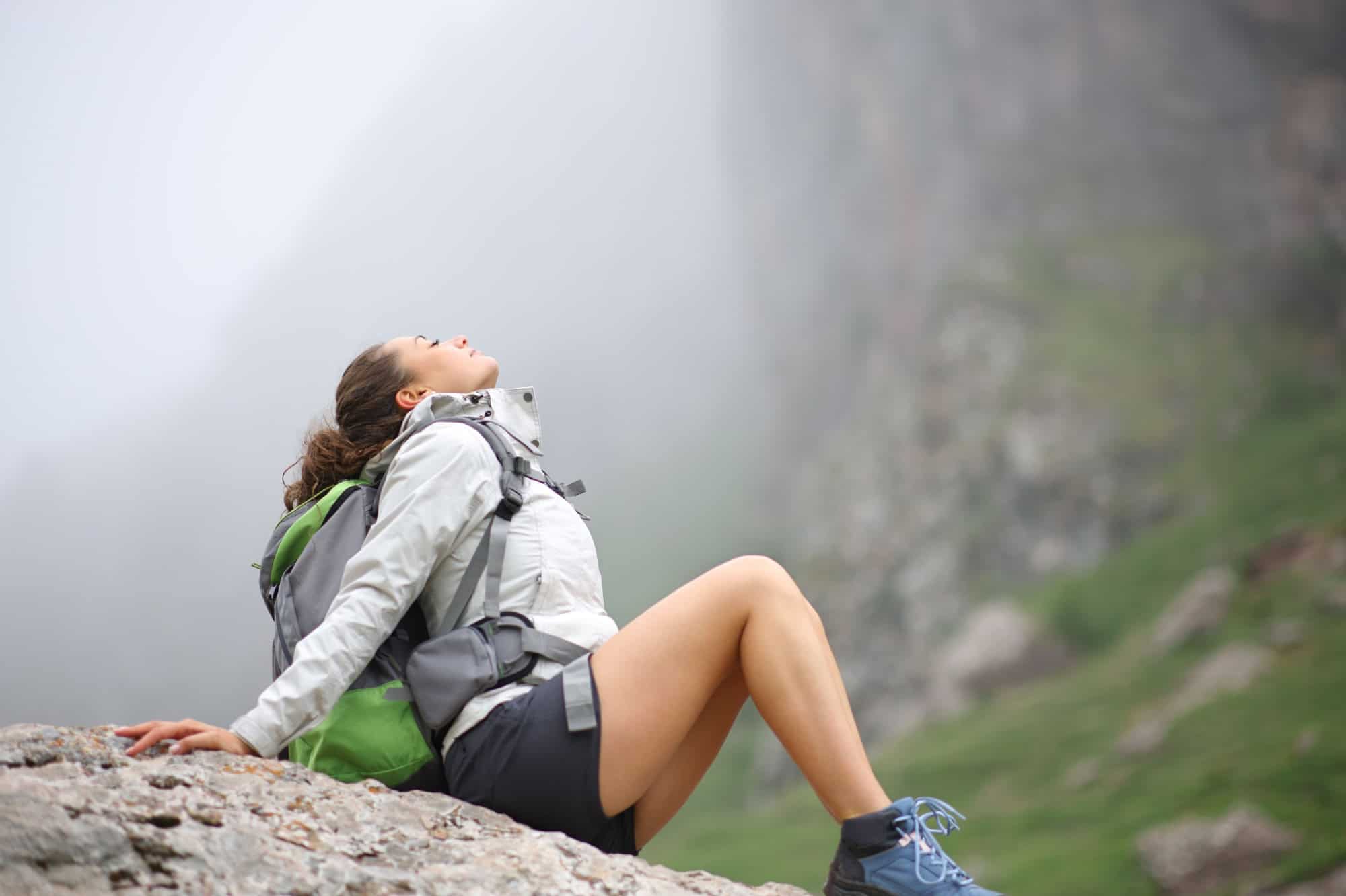 Profile of a hiker resting and breathing fresh air sitting in a rock in the mountain a foggy day