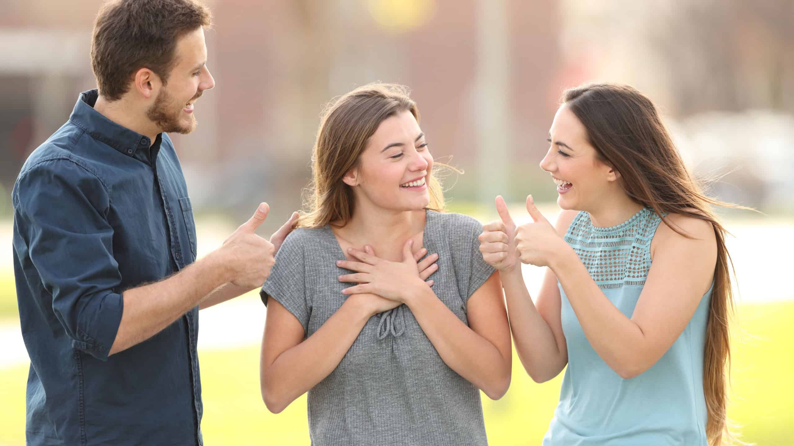 Two friends congratulating a happy girl standing in the street