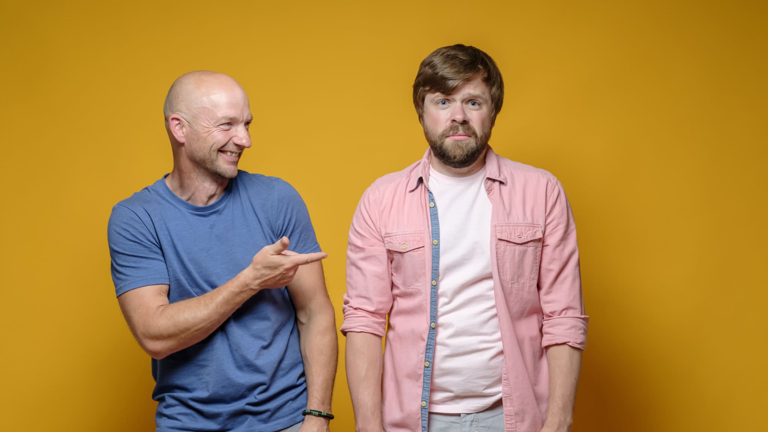 Bald man taunts his upset, unhappy friend and mockingly points finger at him. Bad joke.