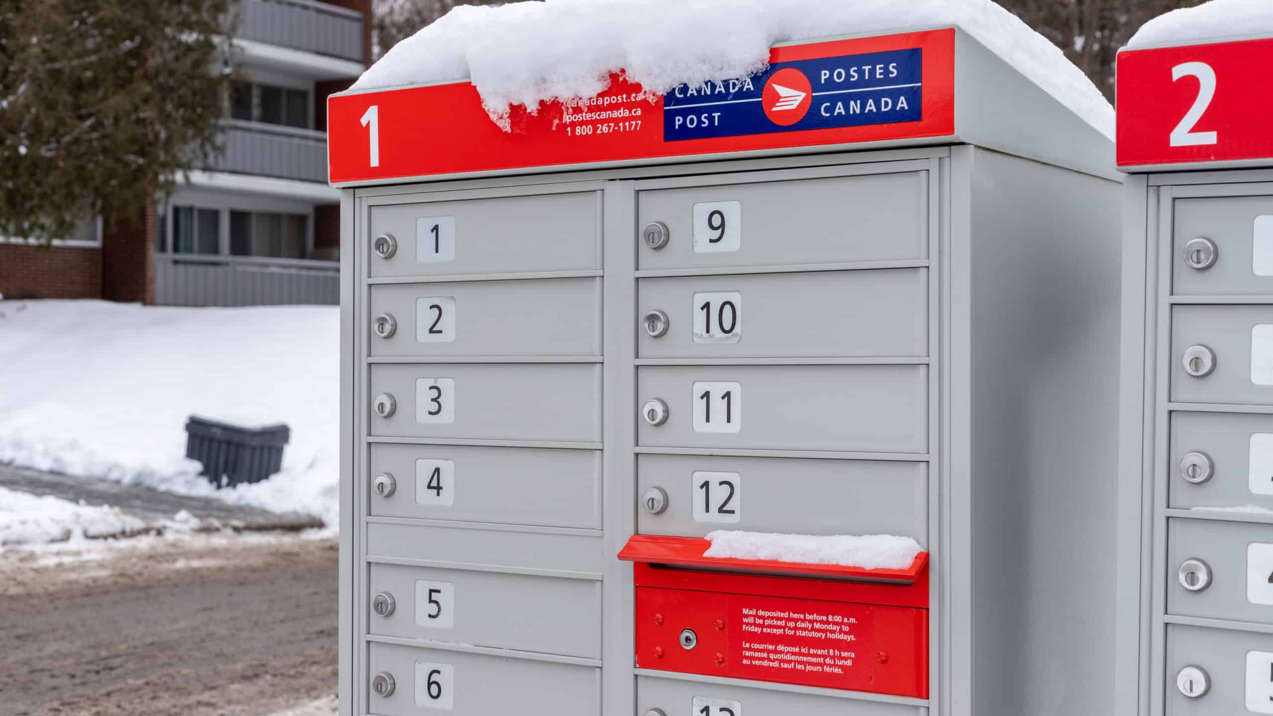 Canada Post mailbox with red sign in English and French near house in winter season