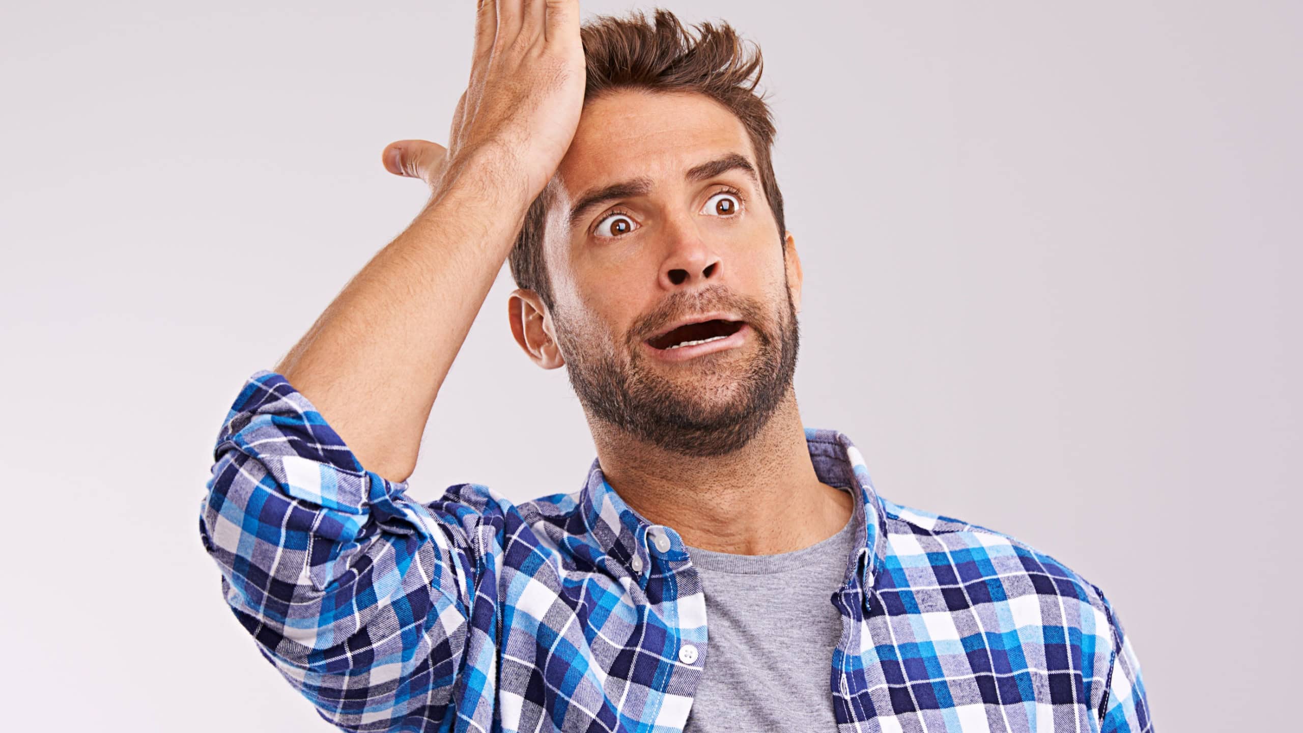 Duh. Studio shot of a young man looking forgetful against a gray background.