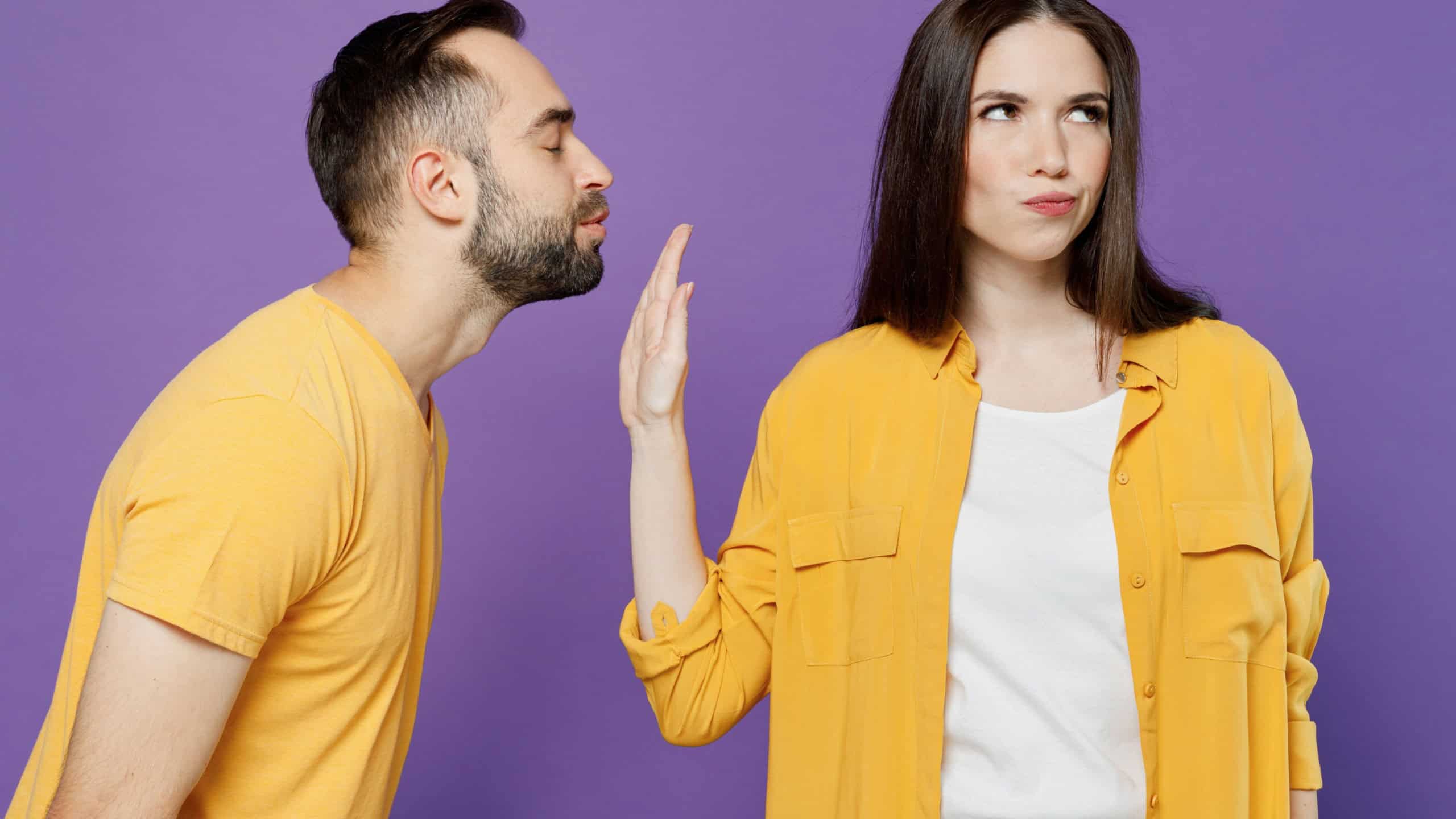 Young sad couple two friends man woman 20s together wear yellow casual clothes guy try want kiss woman but she doing stop palm gesture and does not want it isolated on plain violet background studio.