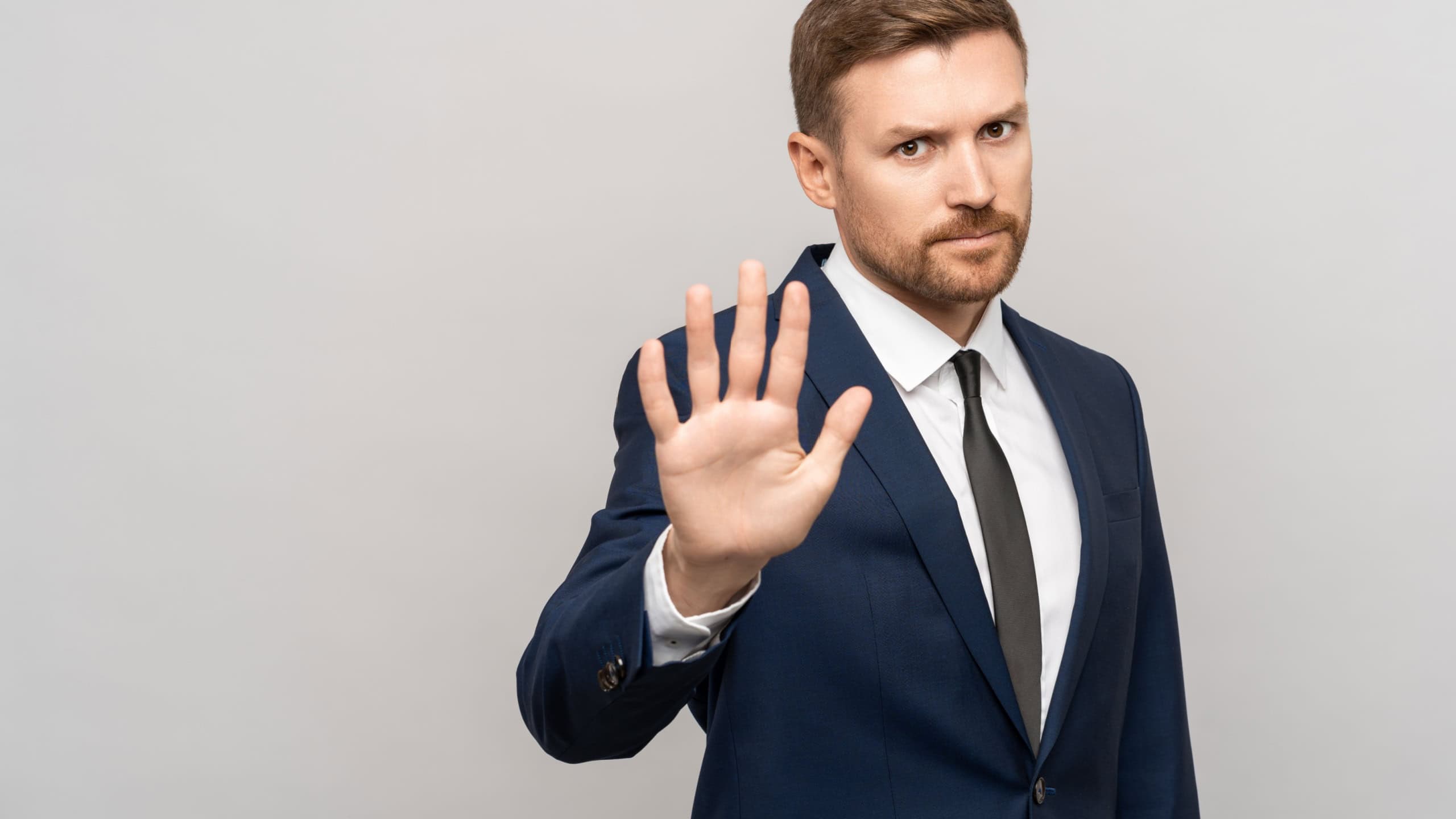 Serious businessman showing stop hand gesture on grey background with copy space. No sign, not accepting deal in office at work, canceling contract. Not agreeing to statement or refusing agreement.