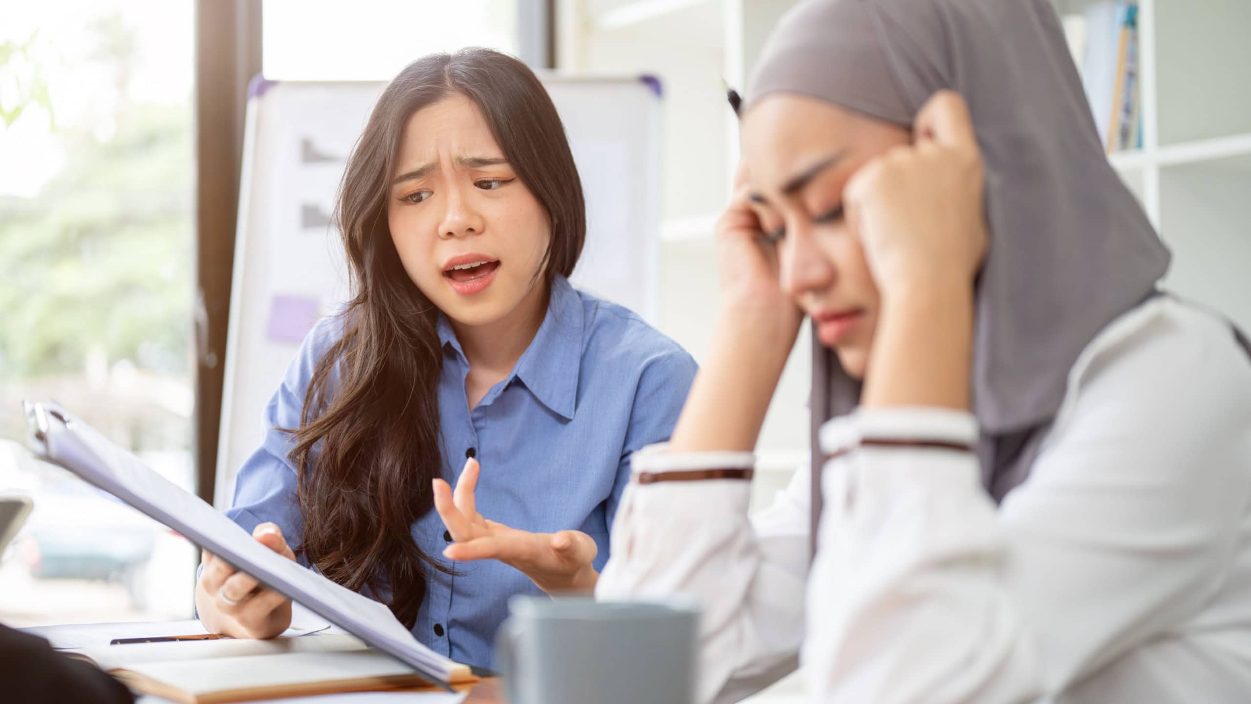 A dissatisfied and serious Asian businesswoman is complaining about the project's mistakes to her Muslim employee or colleague during the meeting.
